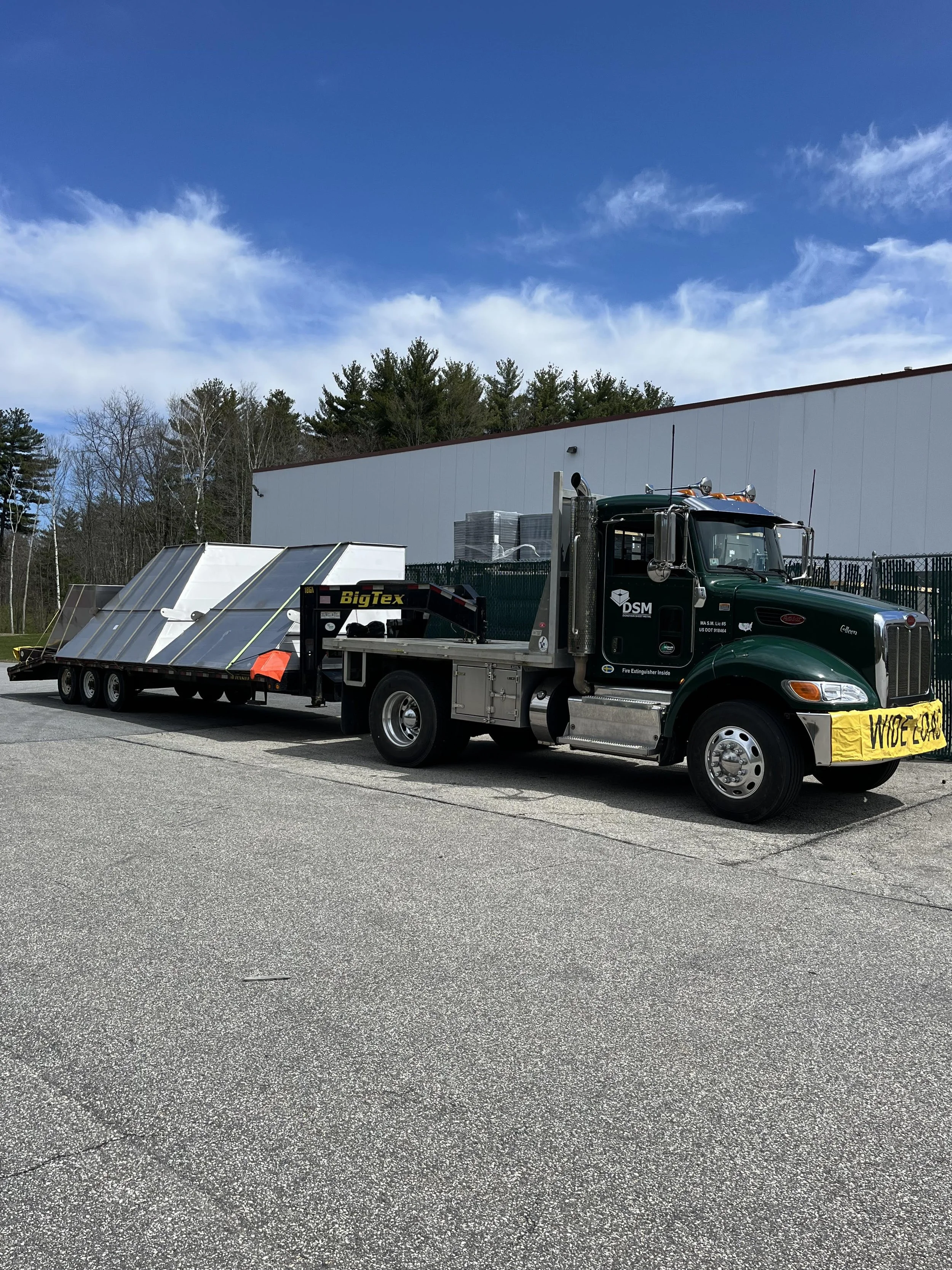 Large black truck parked on asphalt, attached to a trailer with solar panels, and a yellow safety barrier on one side.