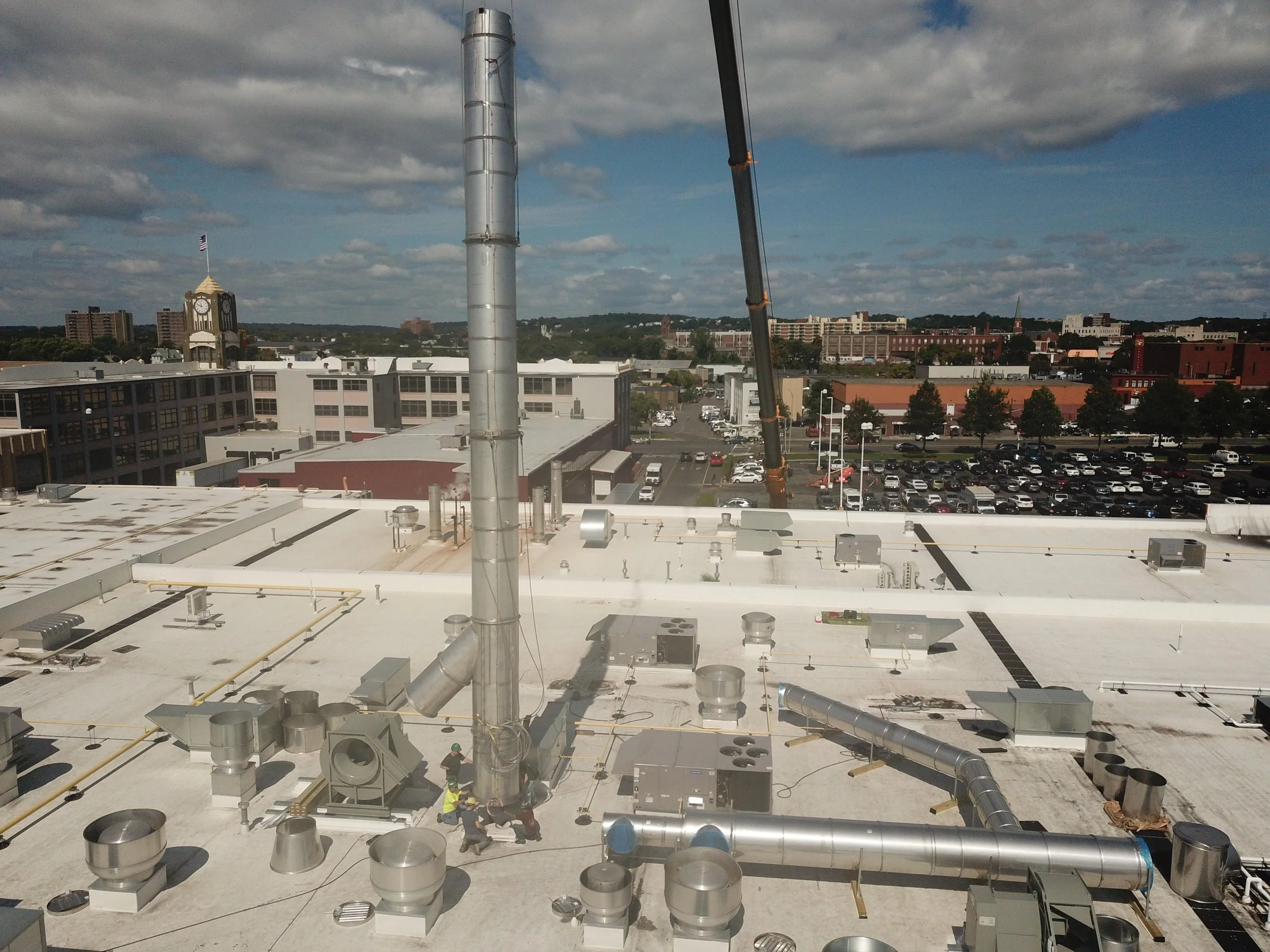 View of a rooftop with various HVAC and ventilation systems under a partly cloudy sky, with a cityscape in the background.