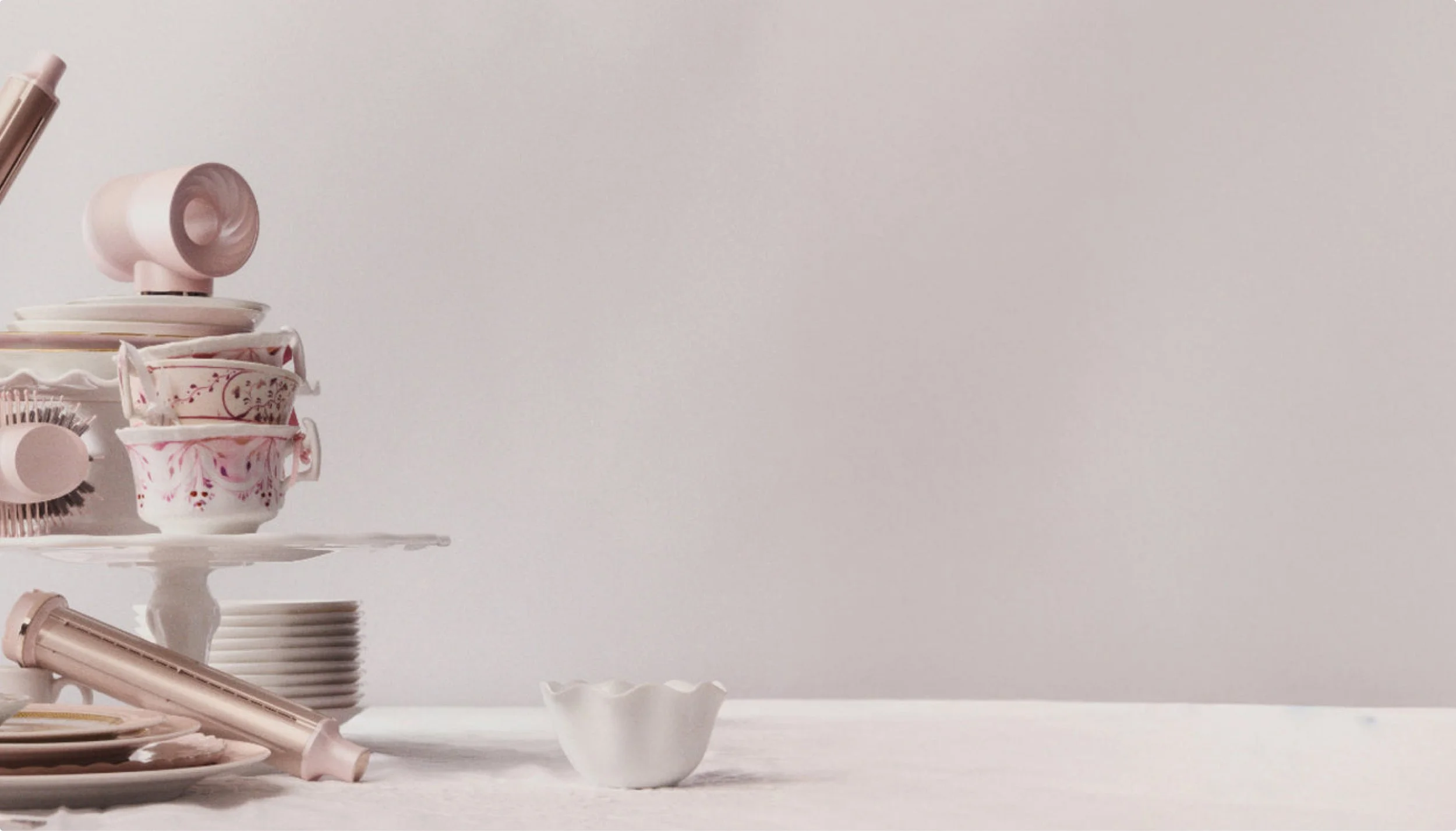 A display of pink and white porcelain cups, saucers, and bowls on a white cake stand and table, with some stacked and others arranged decoratively.