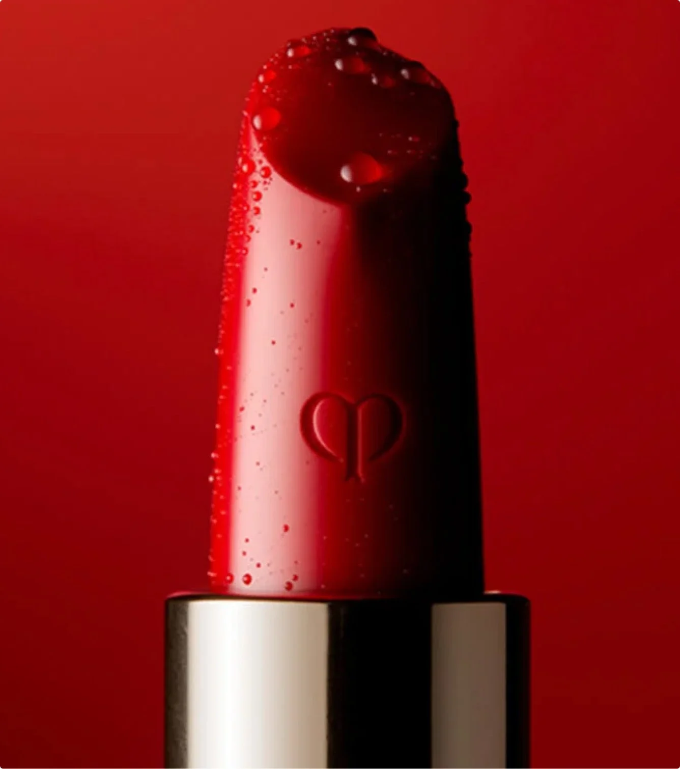 Close-up of a red lipstick with a heart-shaped design on the side, against a red background.