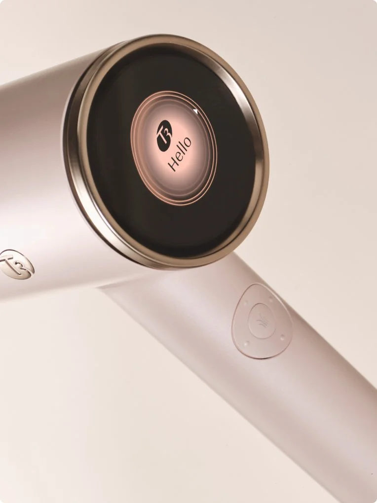 A modern white handheld device with a circular screen displaying the word 'Hello' and the number 13, with a metallic ring around the screen and a speaker button on the handle.