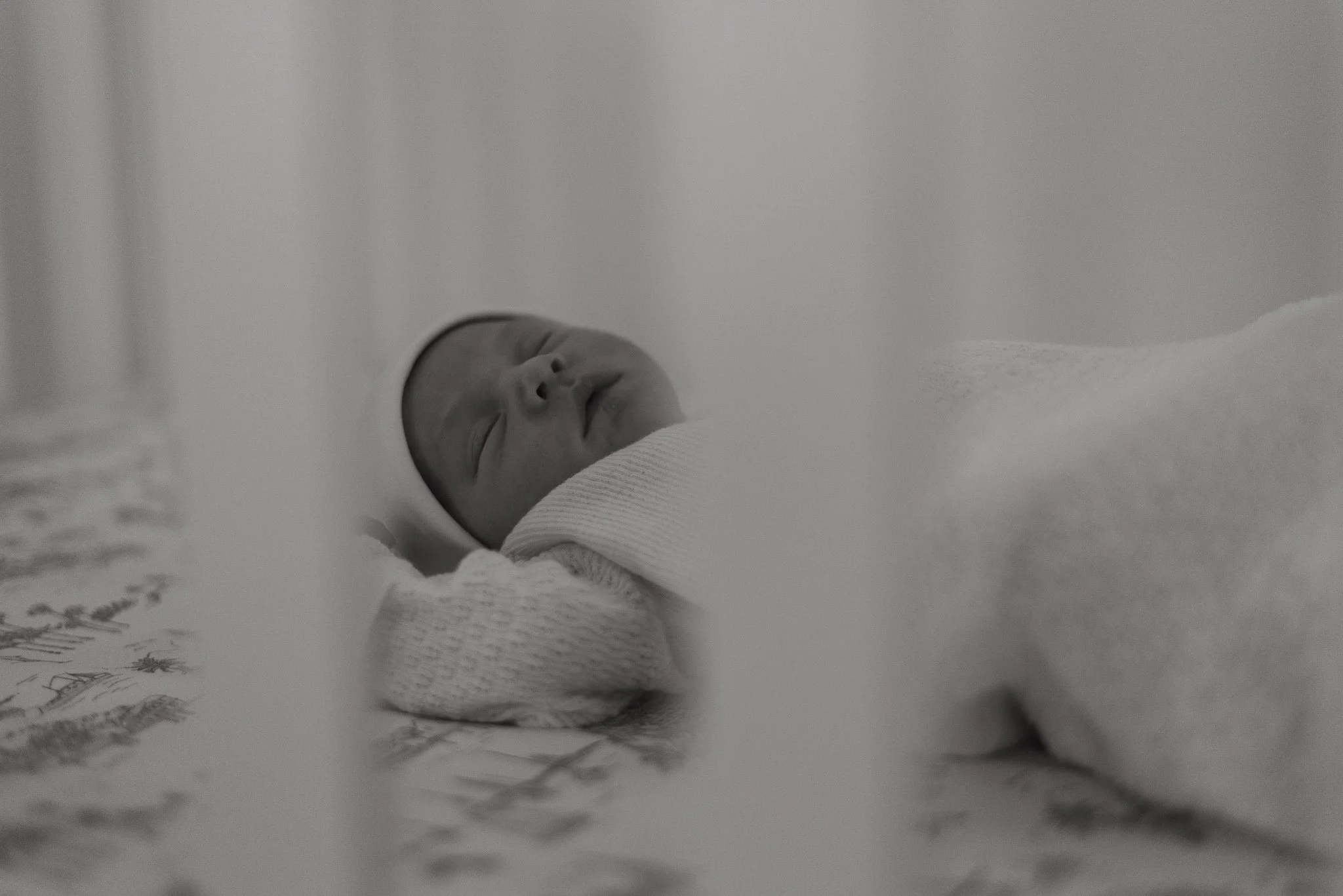 A newborn baby sleeping on a soft surface, with a piece of paper or a book nearby.