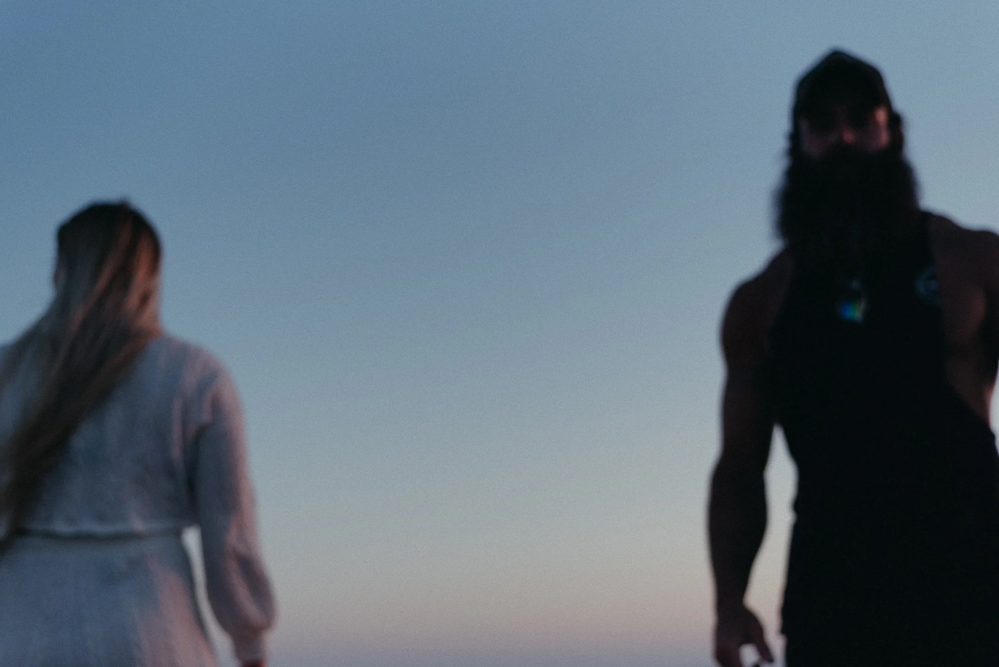 Silhouettes of two people standing outdoors during twilight or early morning, with the sky in the background.
