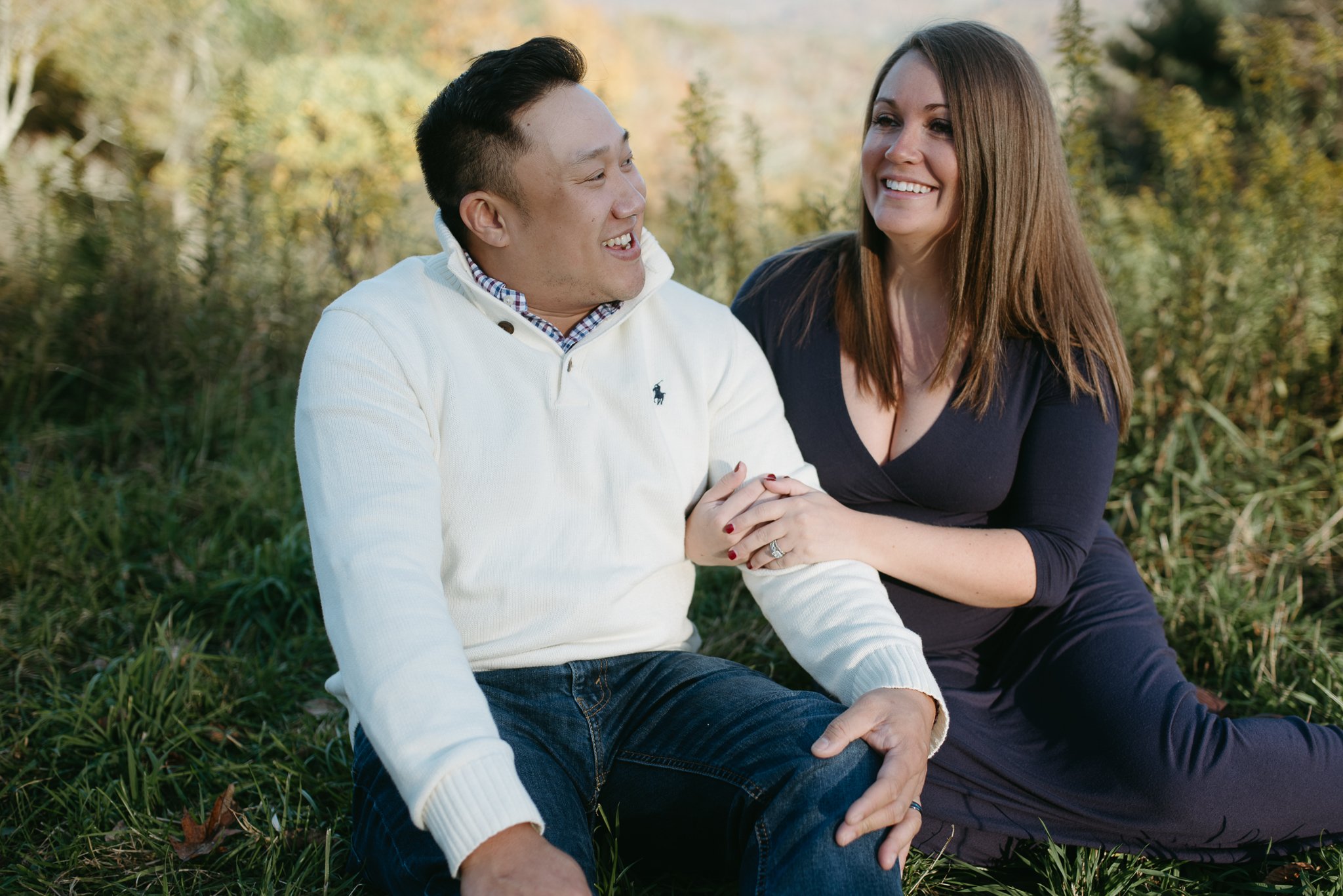 A happy couple sitting together outdoors in a grassy area, smiling and enjoying each other's company on a sunny day.