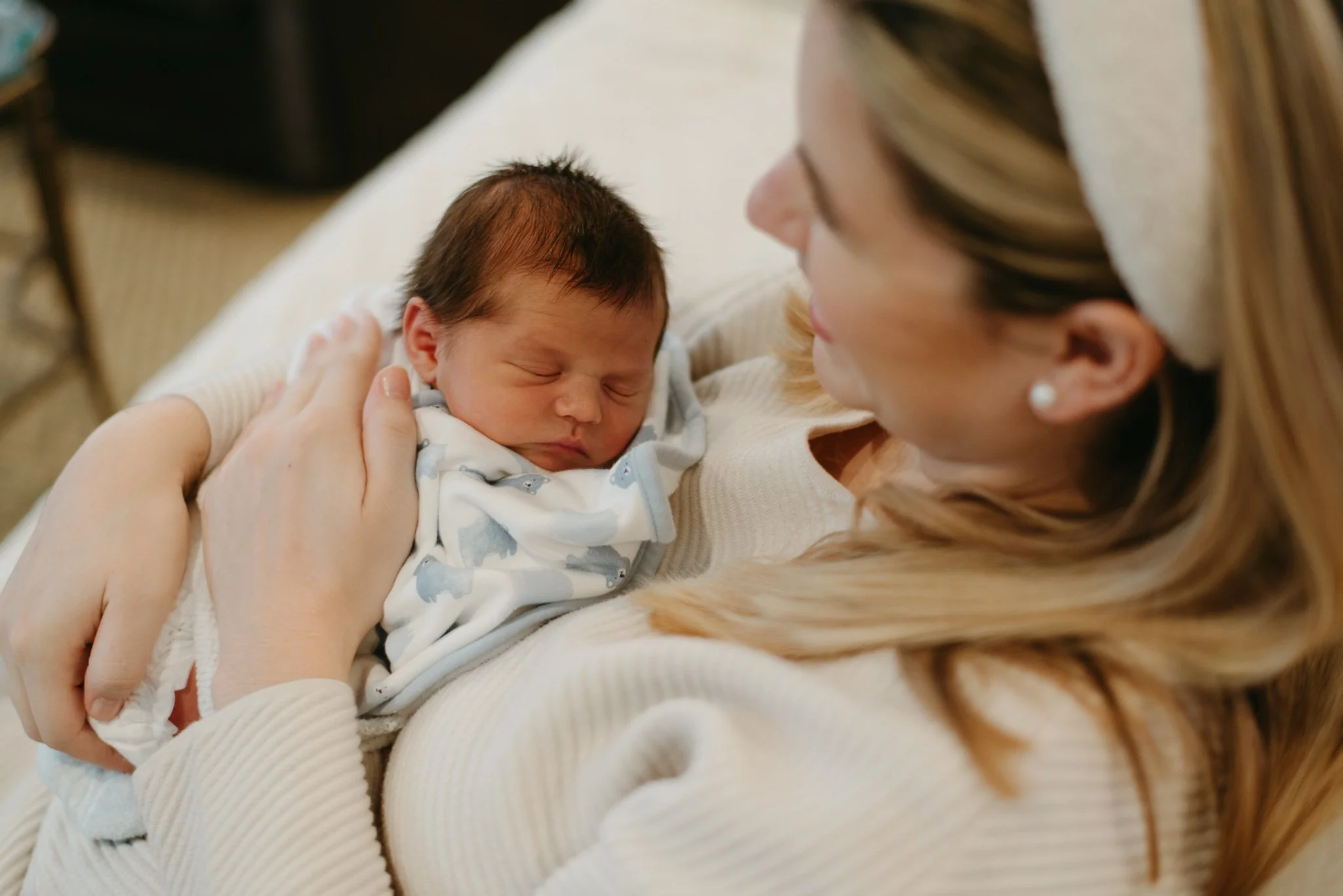 A woman holding a sleeping newborn baby close to her face, gazing at the baby lovingly.