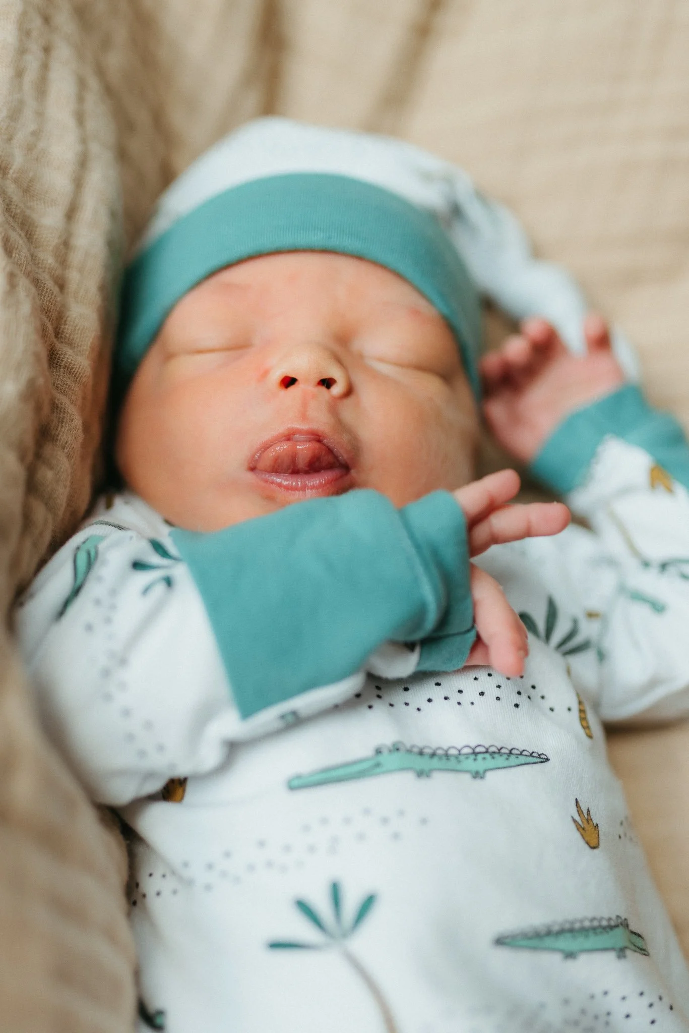 Close-up of a sleeping baby wearing a hat and pajamas with dinosaur prints.