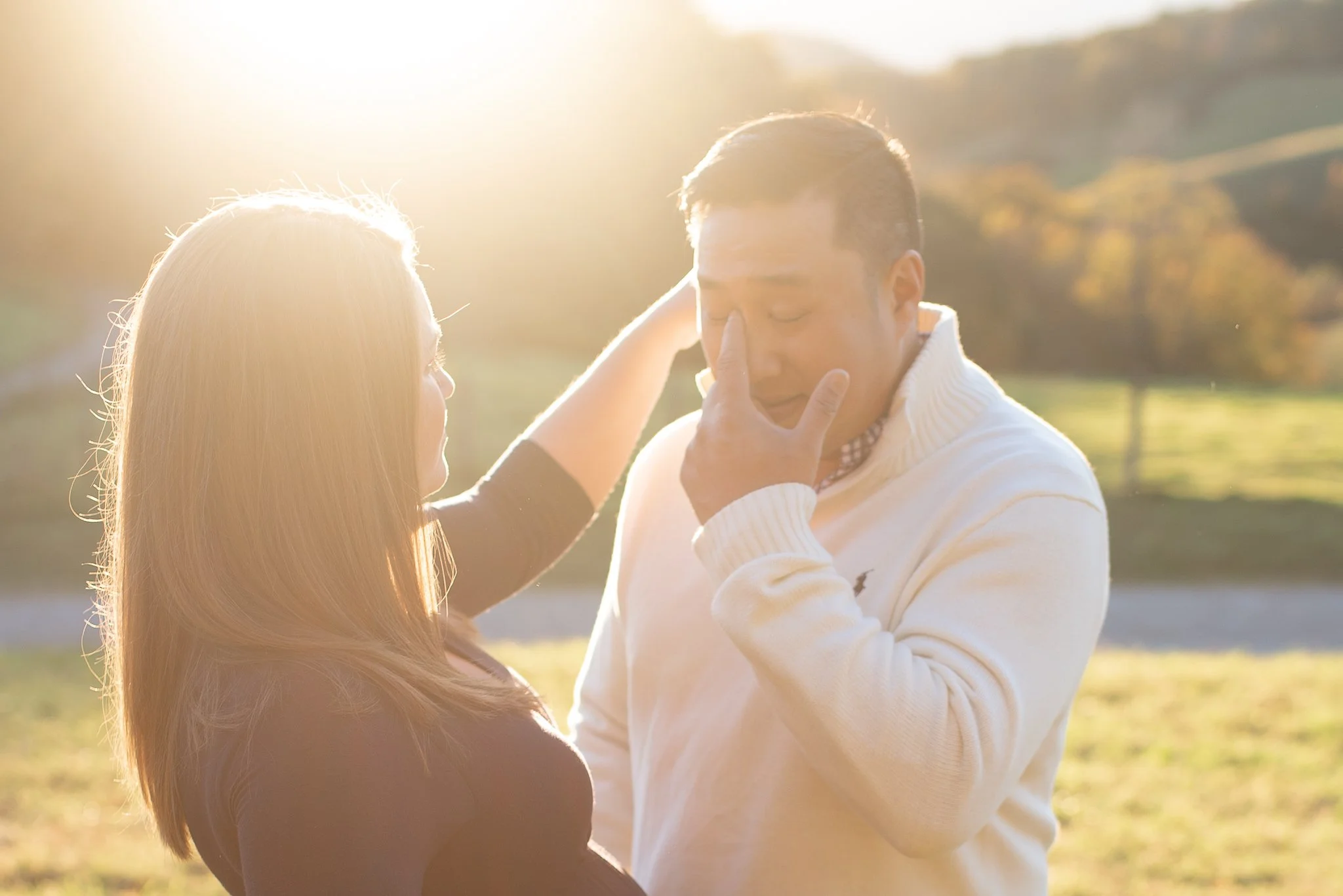 A man and woman sharing an intimate moment outdoors in the sunlight, with the woman touching the man's face gently.