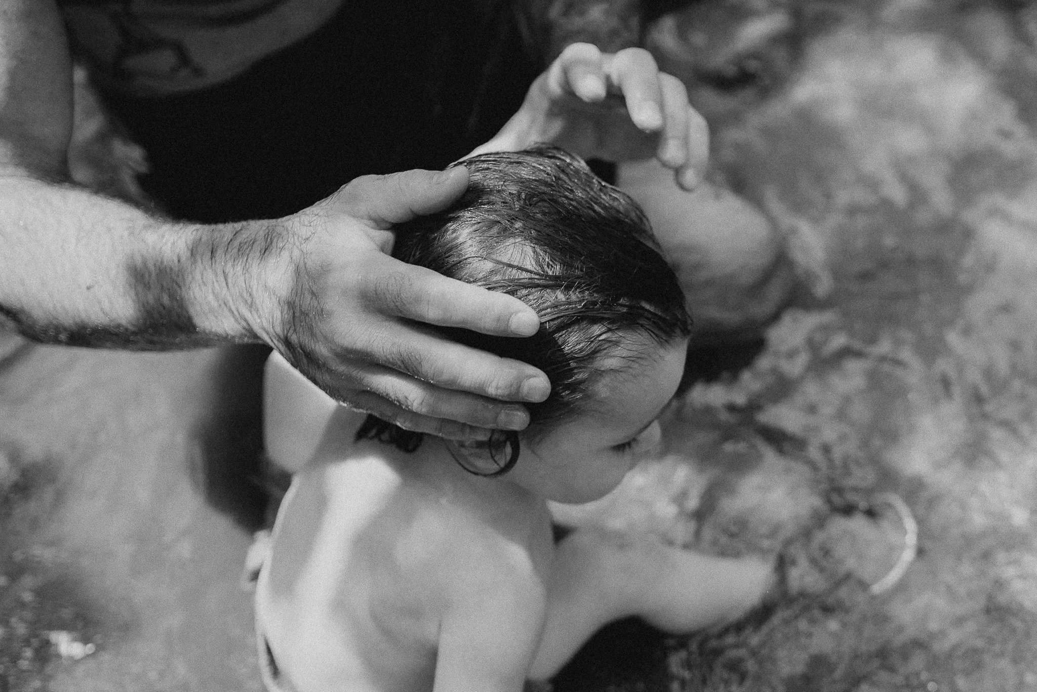 A person giving a baptism or similar religious ritual to a child in water, with hands on the child's head and hair.