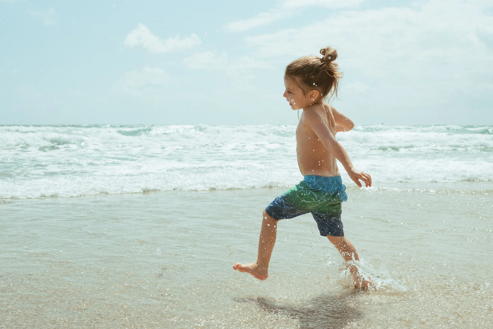 A young boy running and playing in the shallow water at the beach on a sunny day.