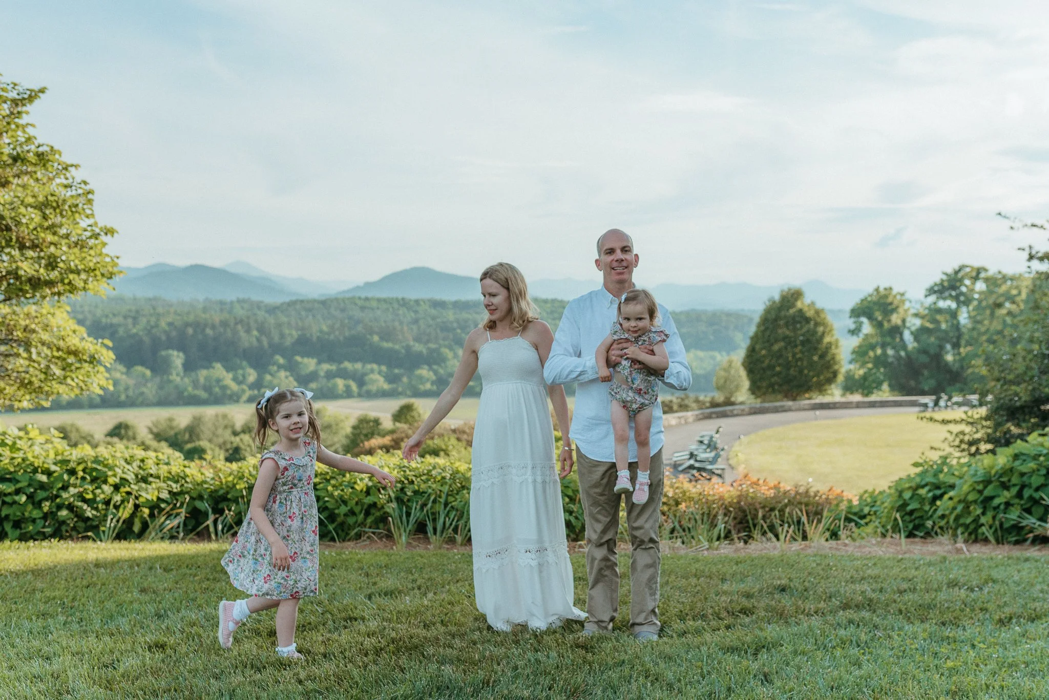 Family walking outdoors with mountains in the background on a sunny day, including a woman, a man, and two young girls.
