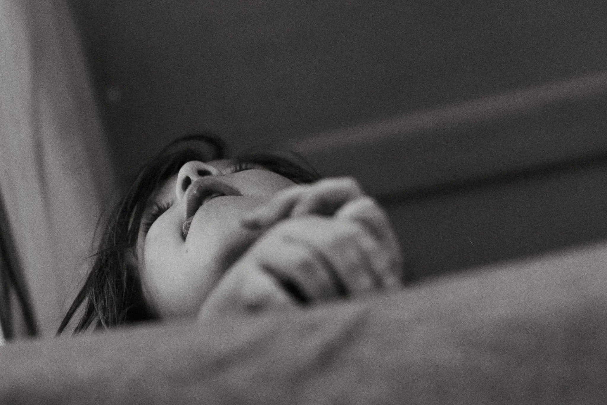 Close-up black and white image of a young woman with long hair lying down and looking upwards, with her hand resting near her face.