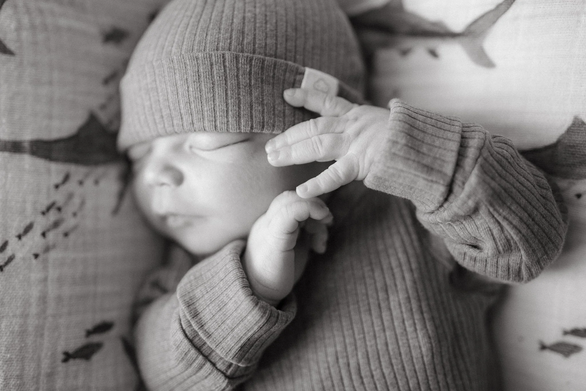 Black and white photo of a baby wearing a knit cap and a long-sleeve top, lying on a blanket with small eyelet holes.