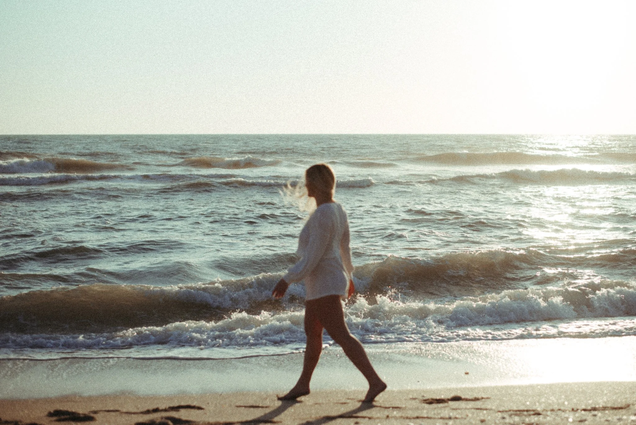 Person walking along the beach with waves in the background during sunset or sunrise.