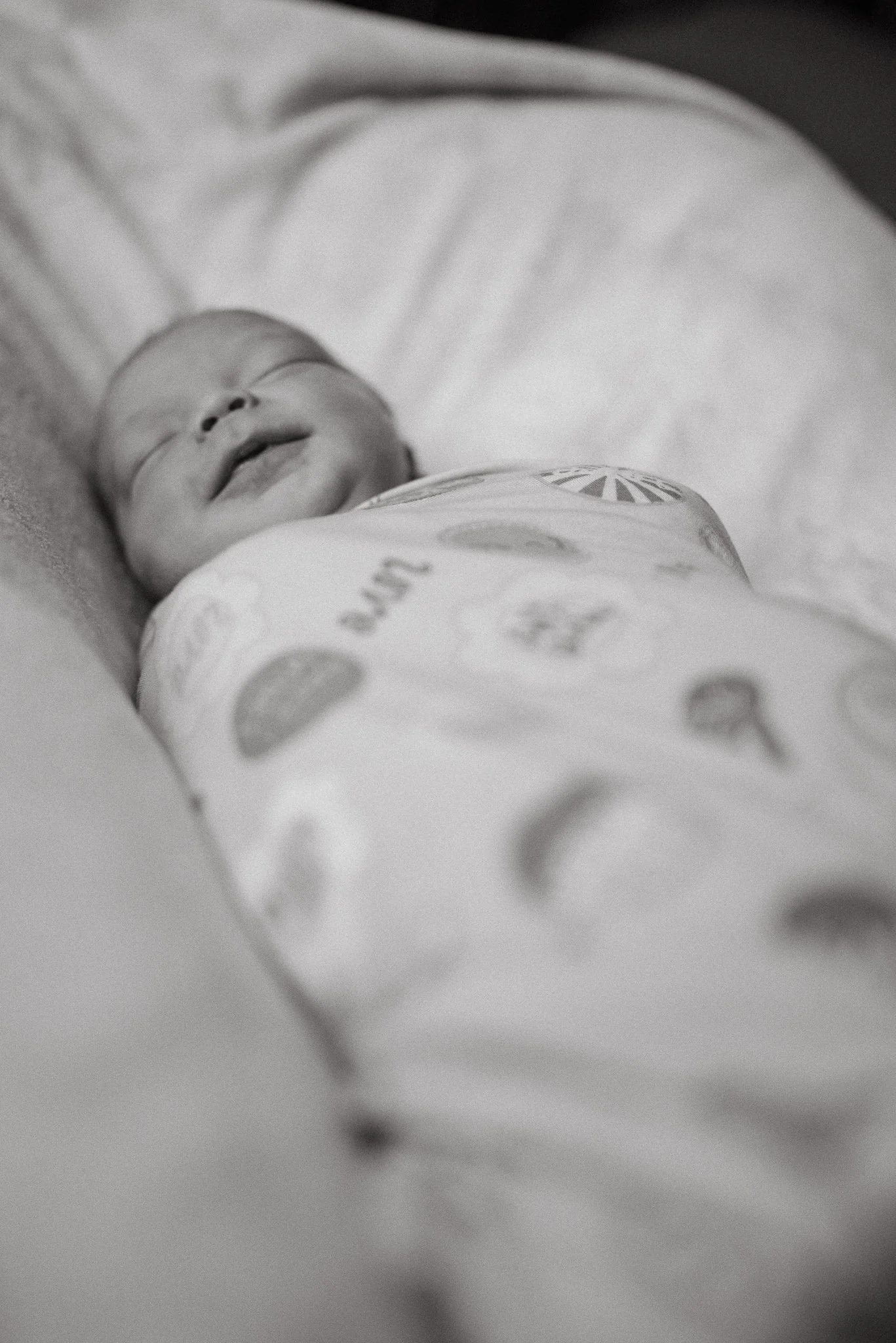 A sleeping baby with closed eyes, lying on a white blanket or sheet, wearing clothing with a circular pattern.