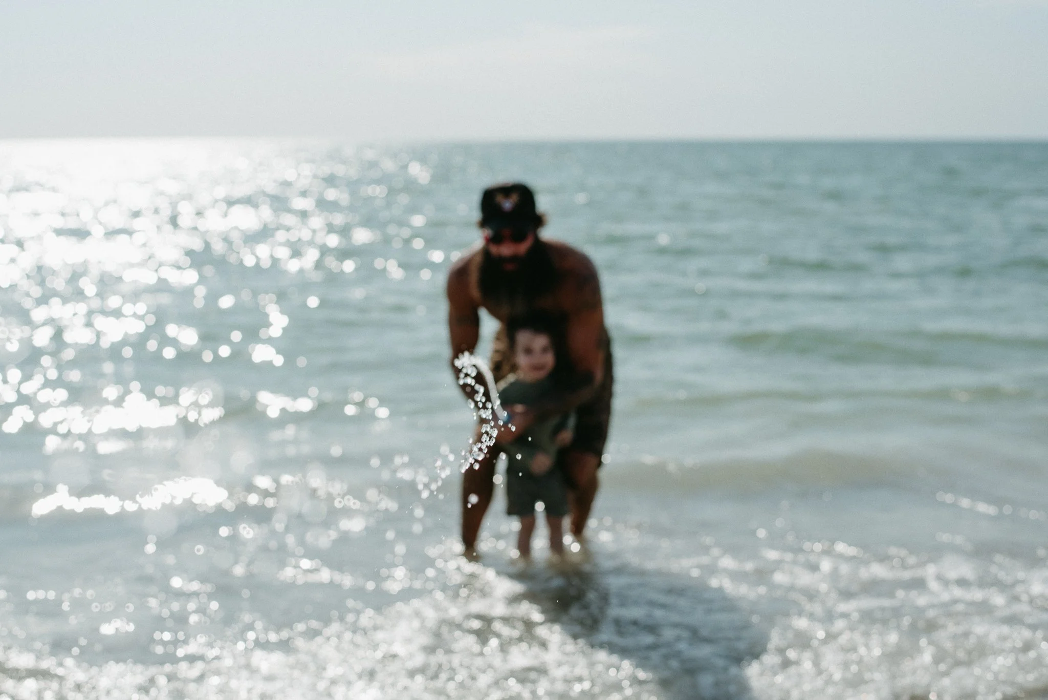 A man and a child playing in the ocean, with the man carrying the child and splashing water as they enjoy a day at the beach.