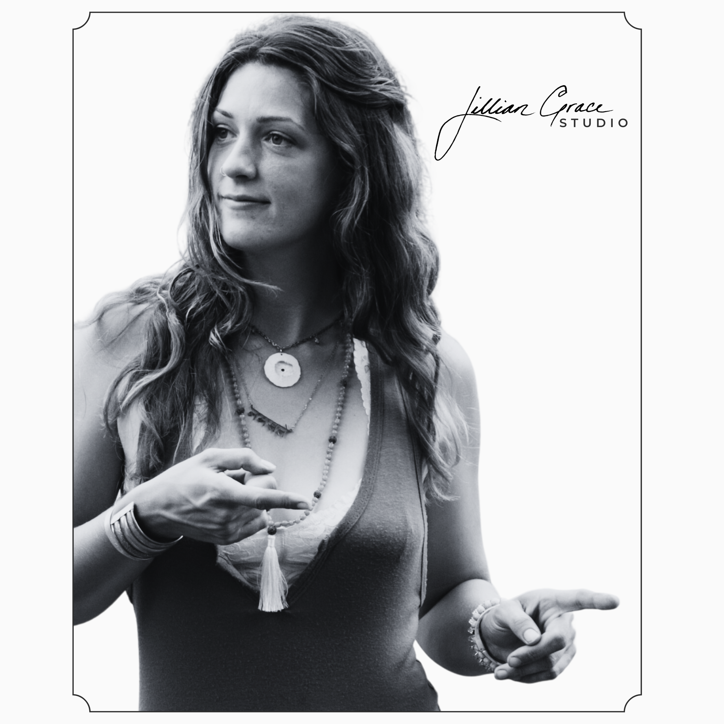 Black and white photo of a woman wearing layered necklaces, bracelets, and a sleeveless top, adjusting her jewelry with one hand. She has long, curly hair and soft facial features.
