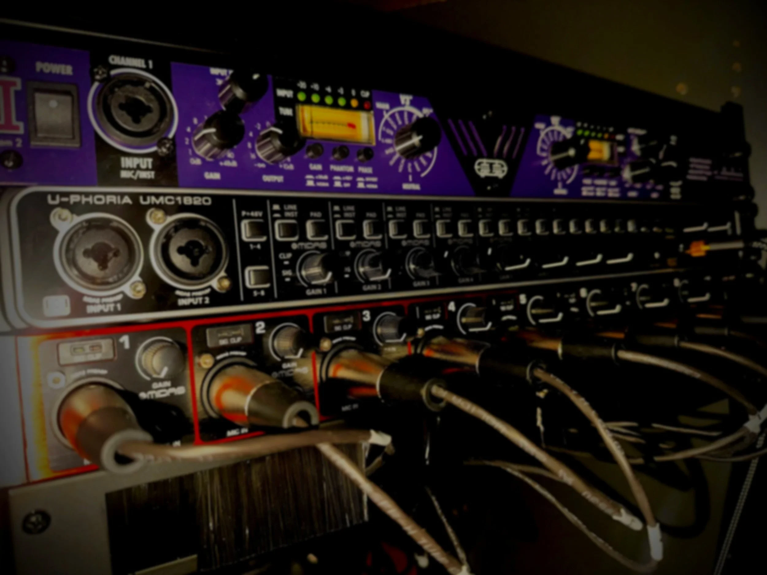 Close-up of audio equipment with multiple knobs, sliders, and cables attached.