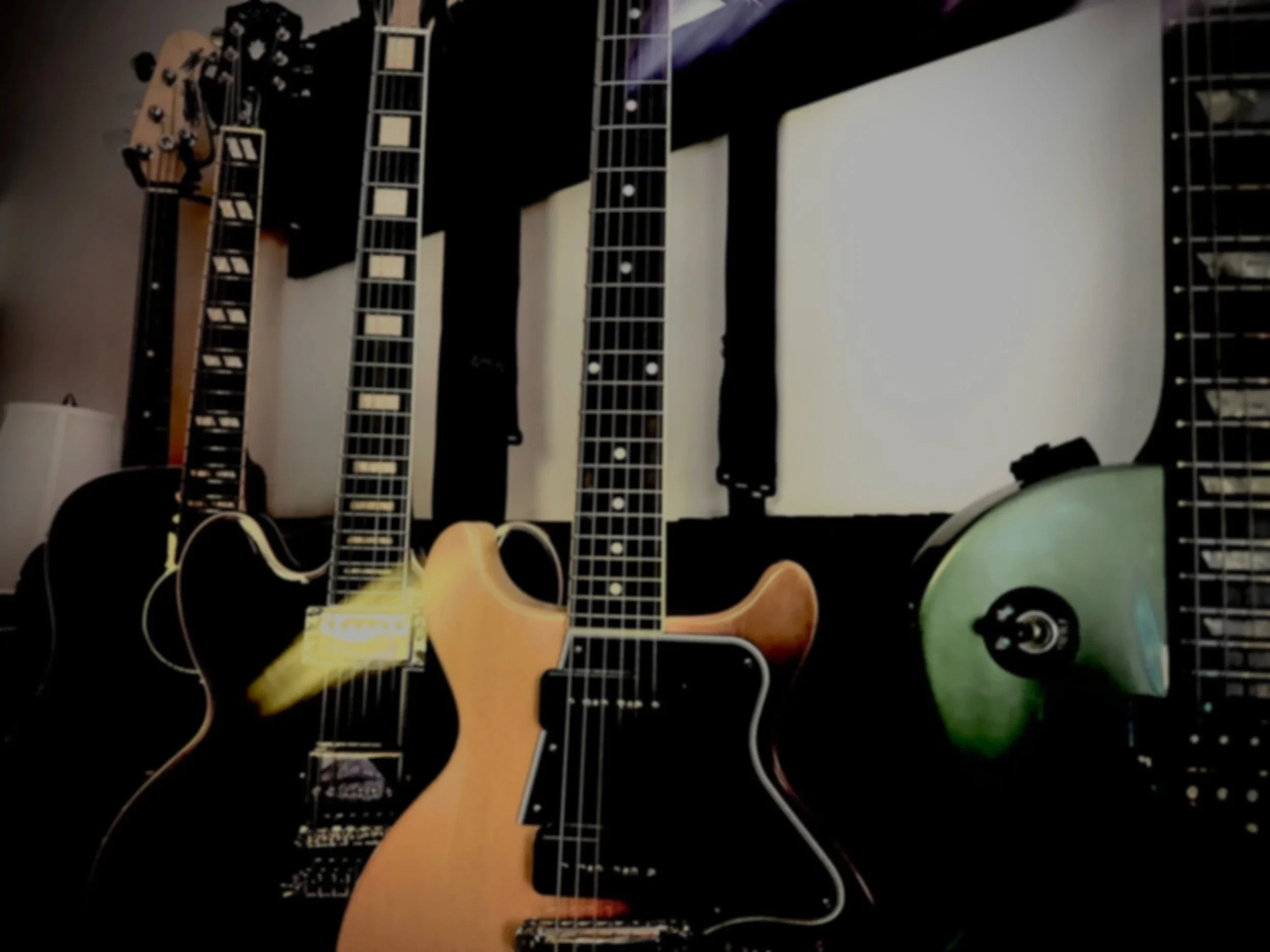 Various guitars hanging on a wall with a light stand and a folding chair beneath them.