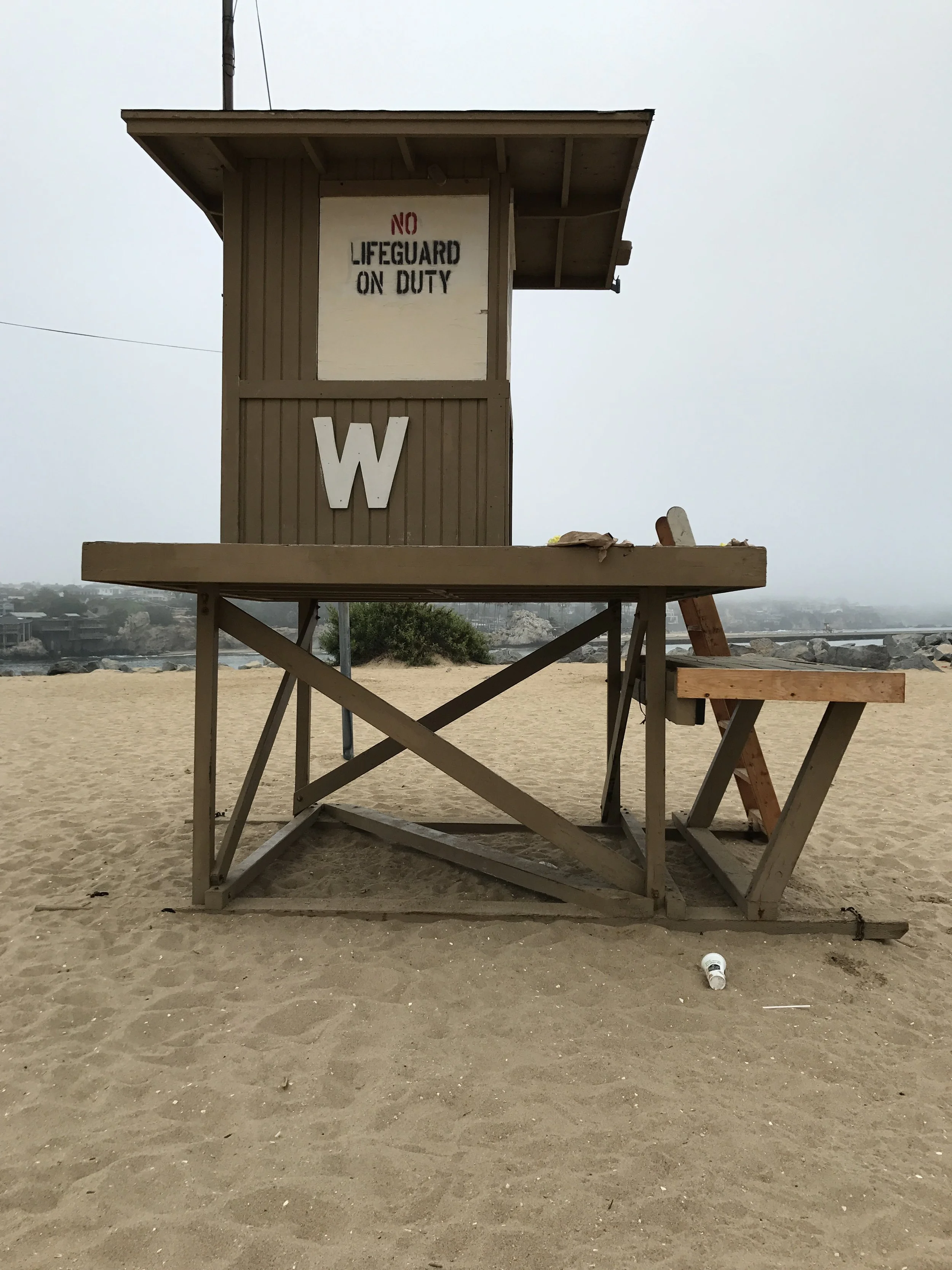 Empty lifeguard tower W at the world famous wedge in newport beach with a sign that reads 'No Lifeguard on Duty' on a sandy beach with a cloudy sky.