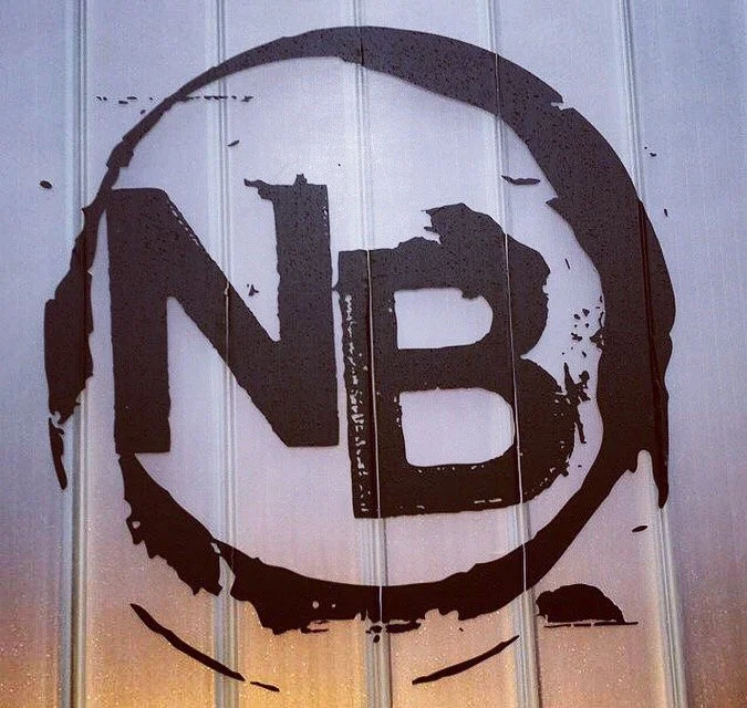 Black and white NB logo for Newport Beach painted on a wooden wall.