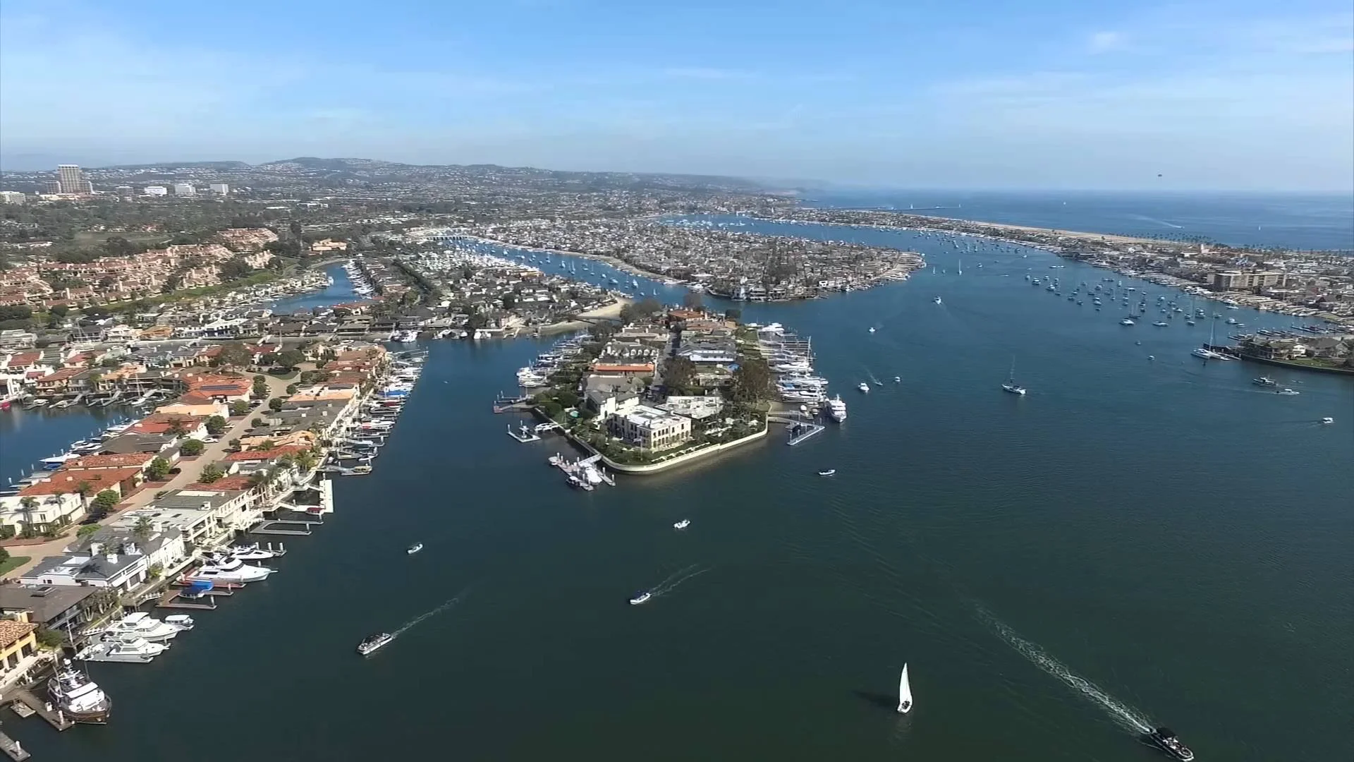 Aerial view of the newport peninsula and lido island, residential and commercial buildings, and boats on the water, near the pacific ocean on a sunny day.