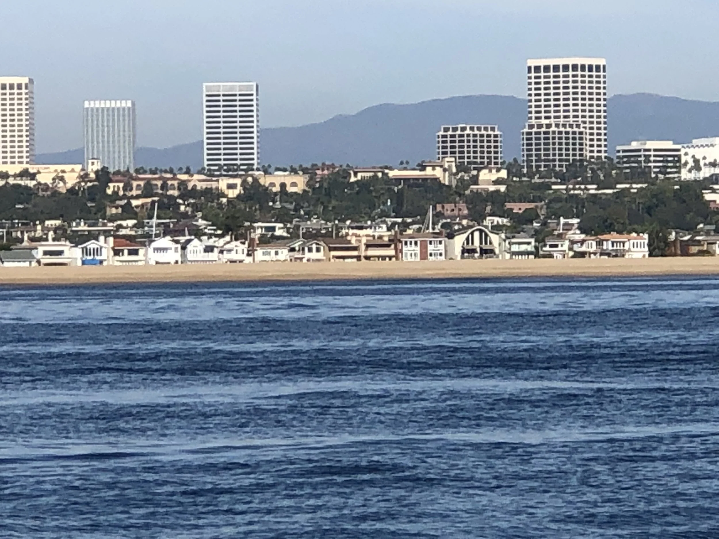 A city skyline with high-rise buildings and mountains in the background, viewed across a body of water in the foreground.