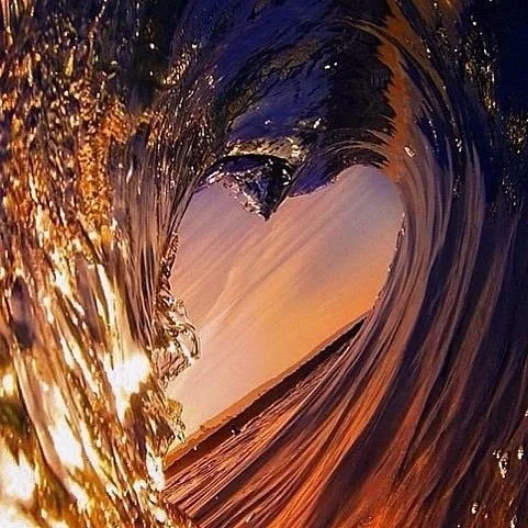 A photo taken through a wave, capturing the sunset and sky in the background with reflections on the water.