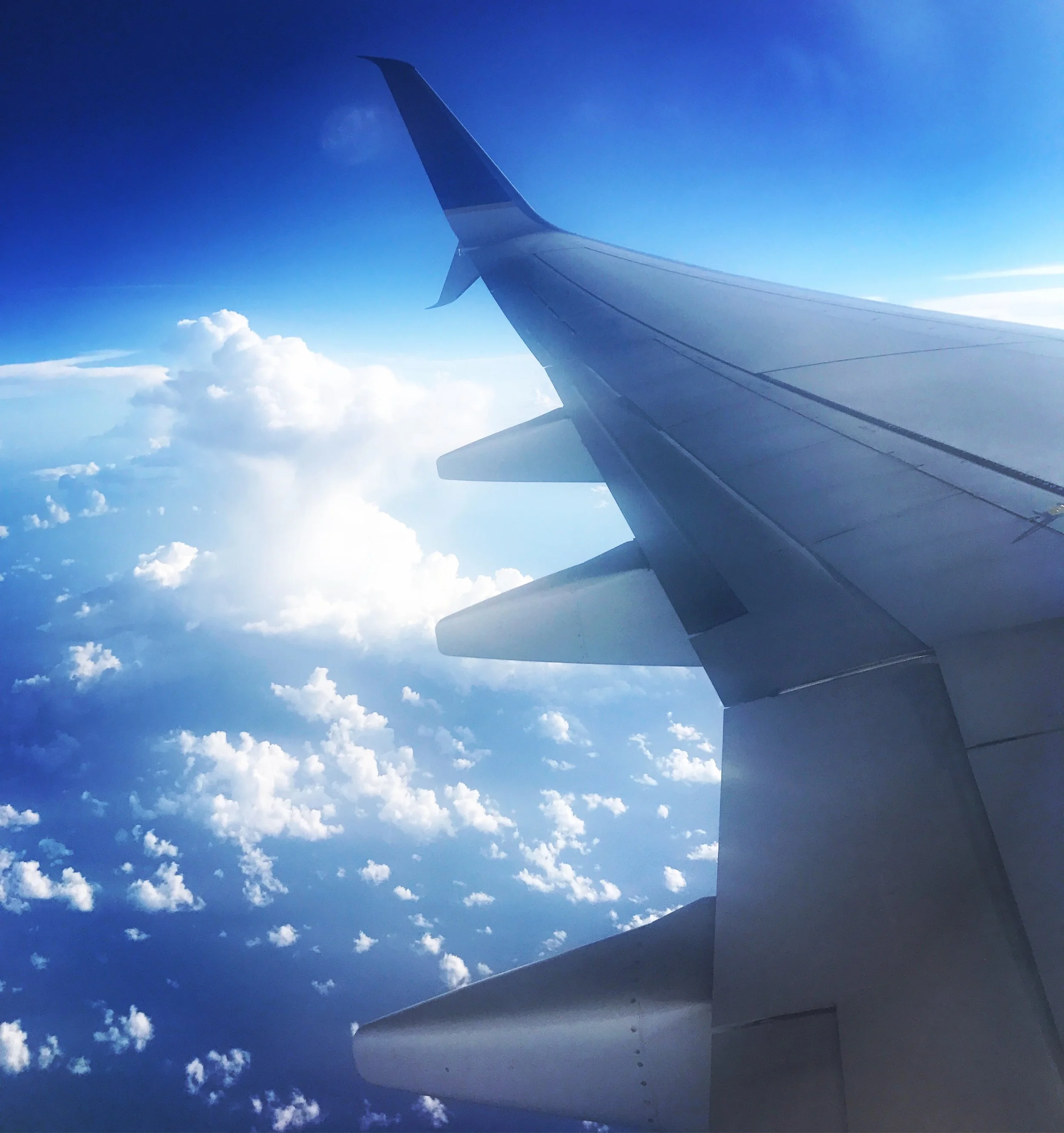 The wing of an airplane flying high above the clouds during daytime above orange county california newport beach.
