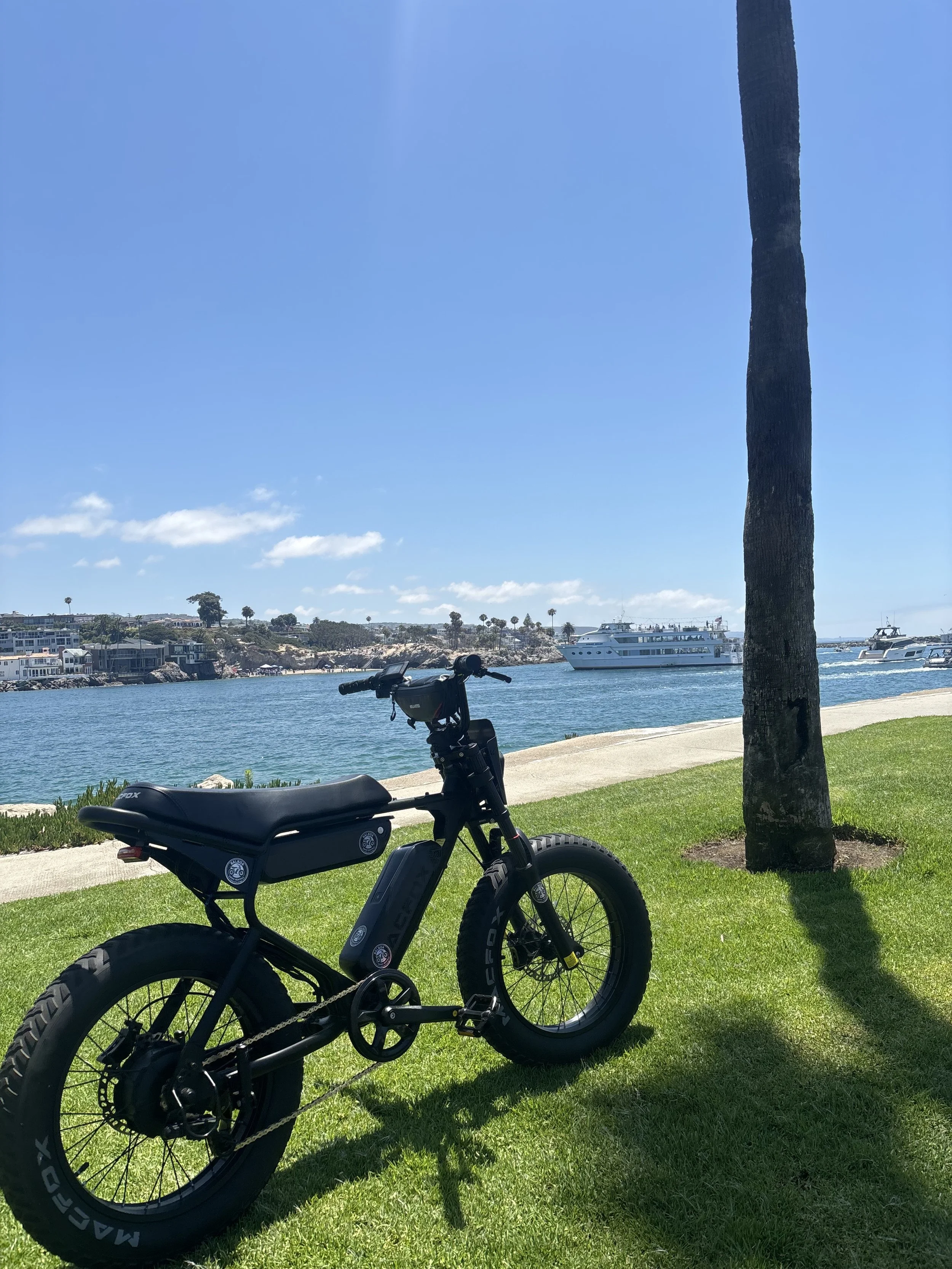 Macfox electric bike parked along Newport Harbor in Newport Beach, California, near luxury yachts and waterfront homes.
