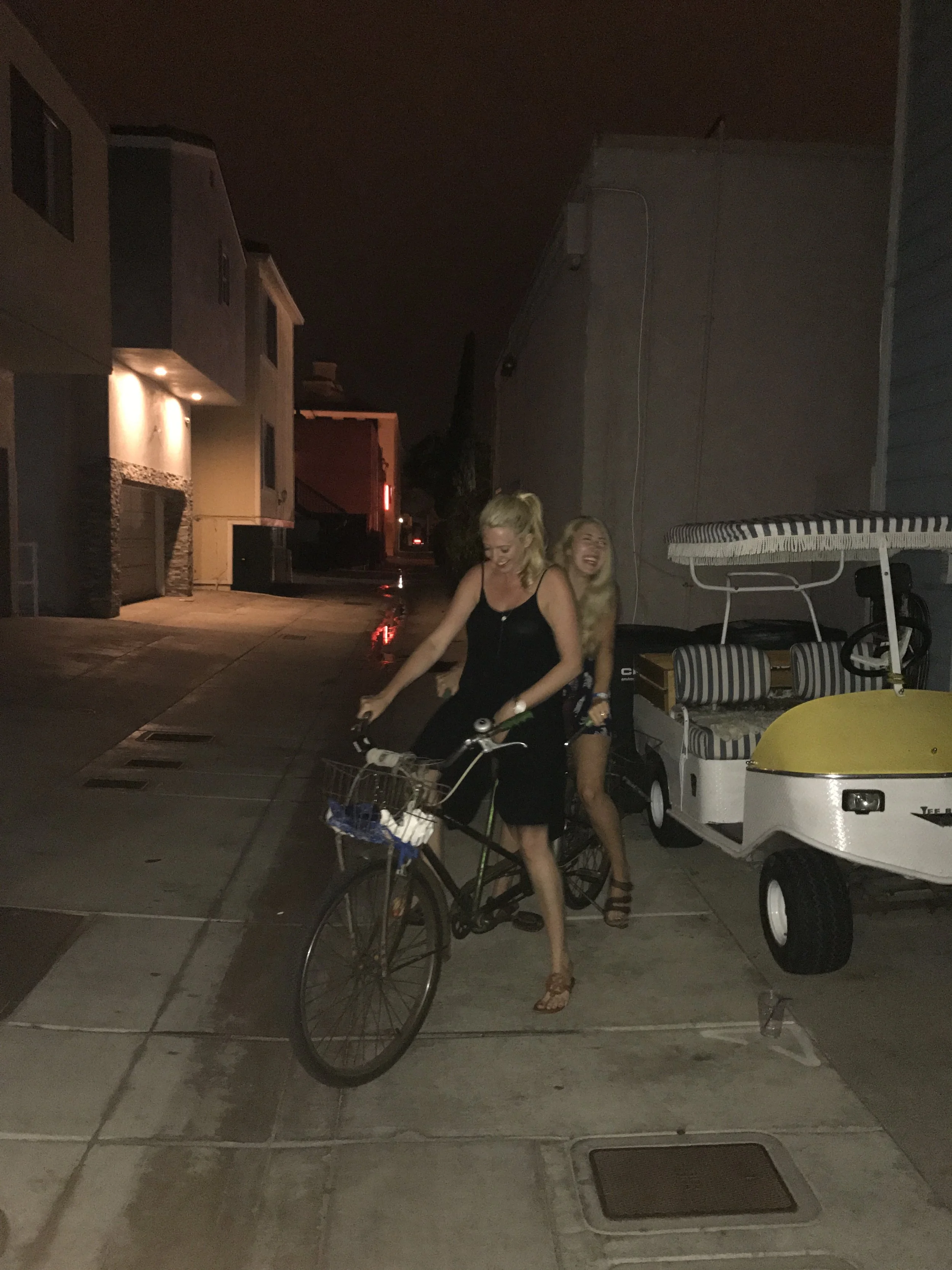 Two women riding bicycles along the Balboa Peninsula in Newport Beach, California, during the evening.