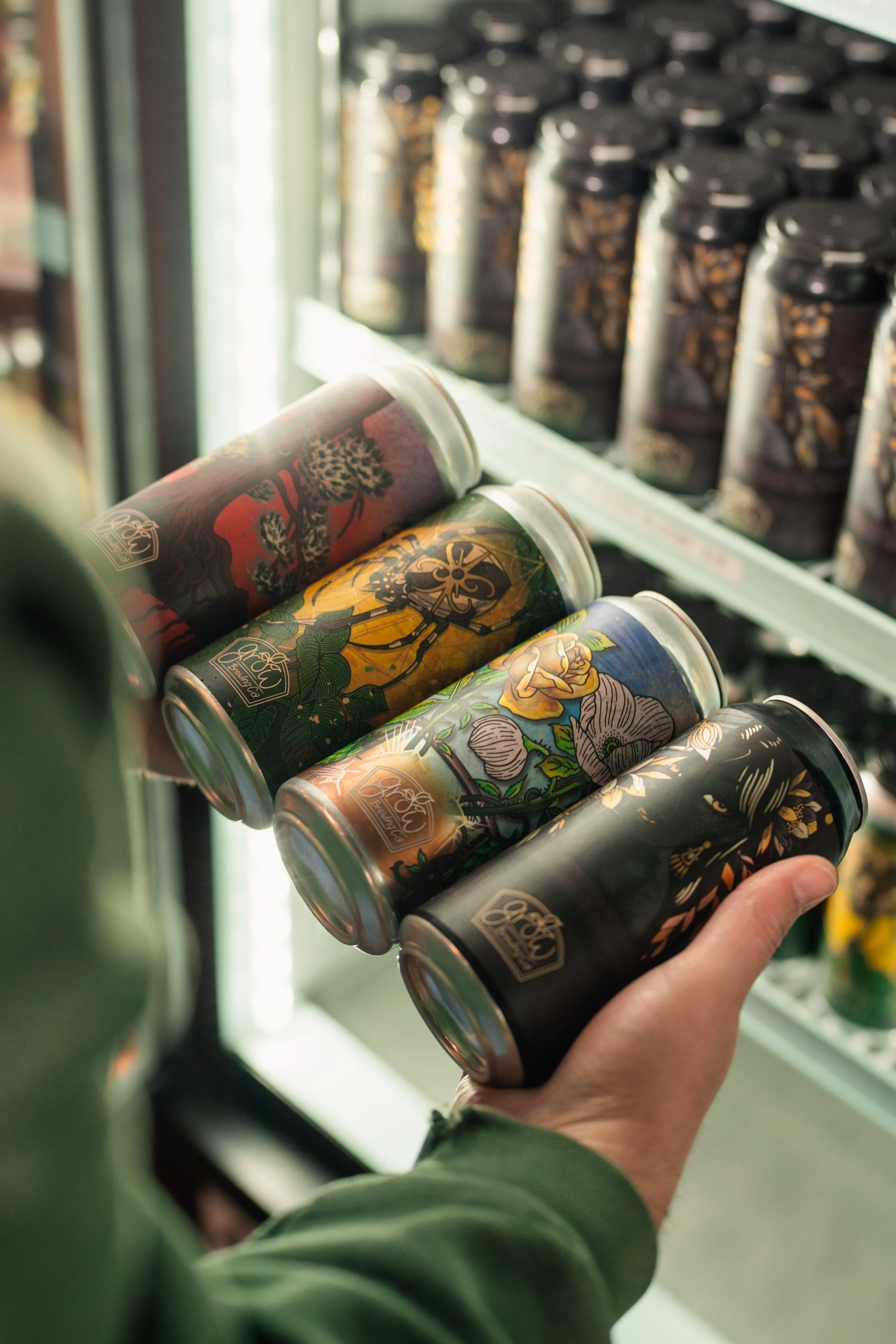 Person holding a can of canned beverage in front of a fridge with other canned drinks.