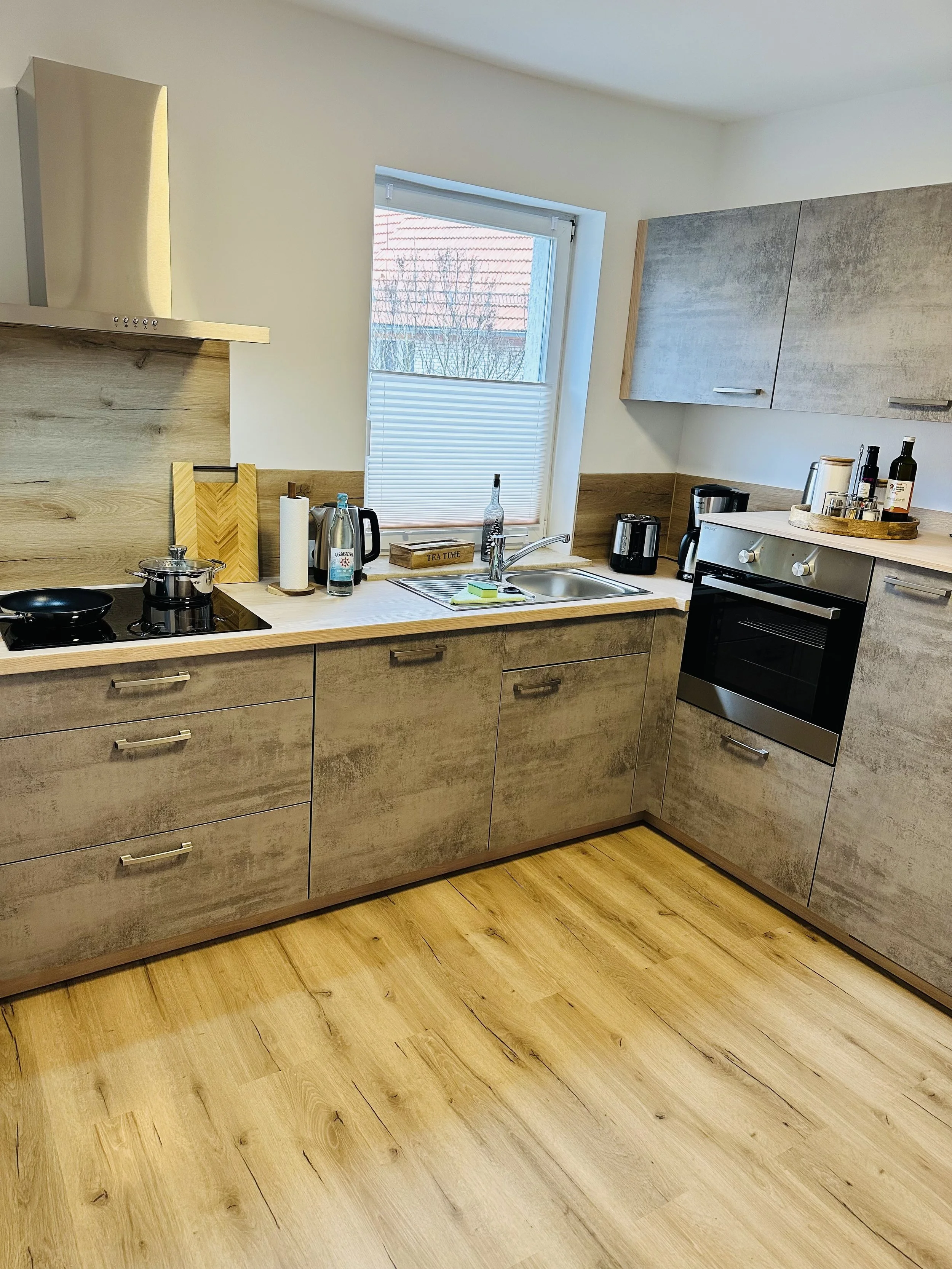Moderne Küche mit Holzmöbeln, Herd, Ofen, Spüle, Fenster und Holzboden.