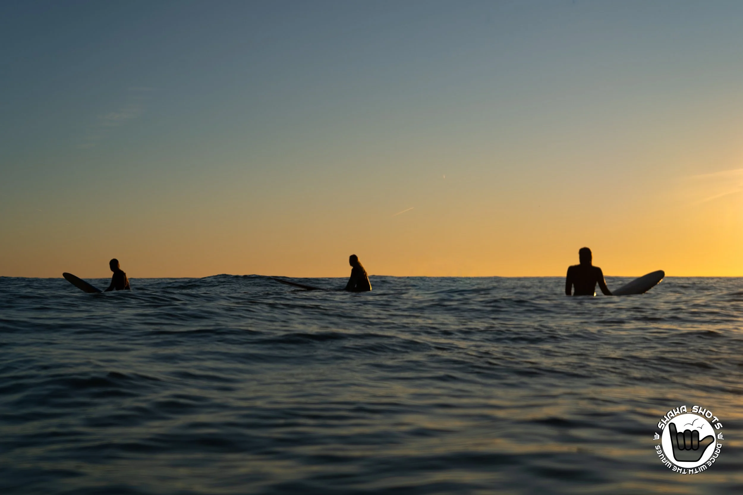 Drie surfers in de zee bij zonsondergang.