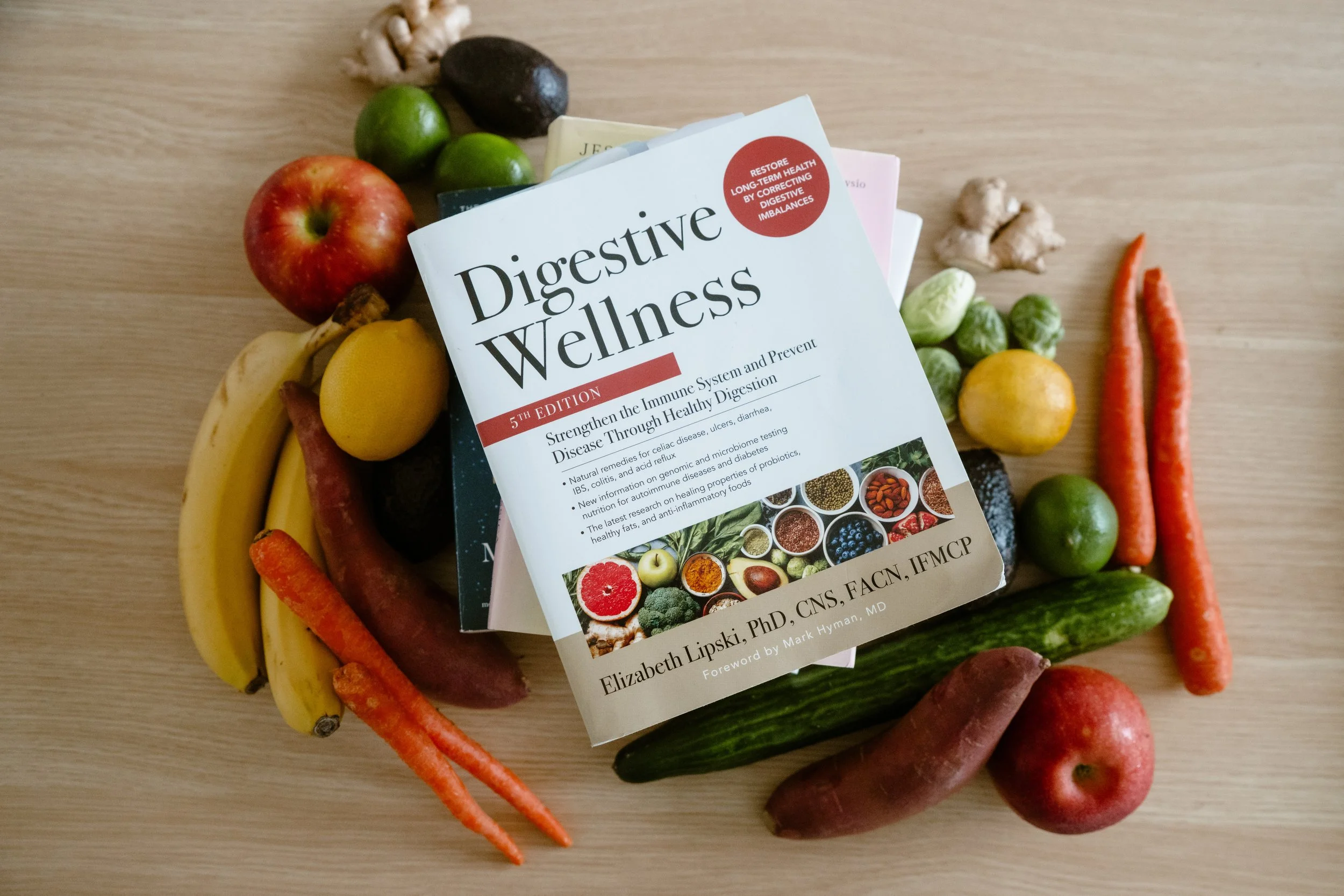A book titled 'Digestive Wellness' surrounded by various fresh fruits and vegetables on a wooden surface.