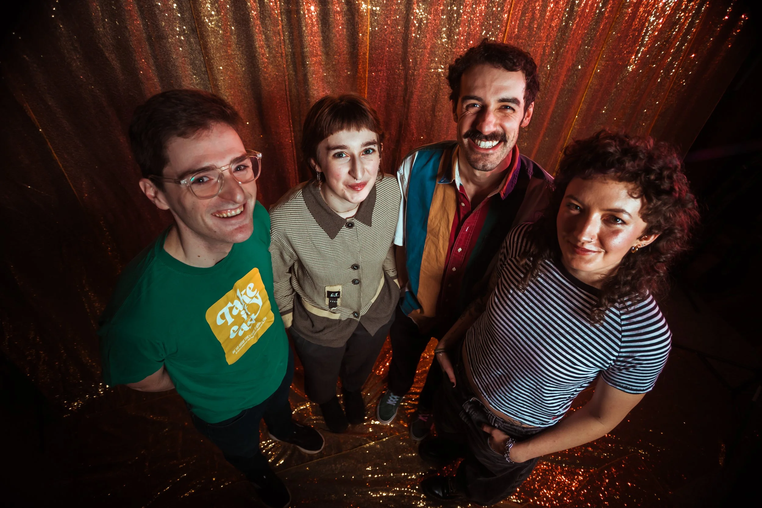 A group of five people standing in a circle, smiling for a selfie against a shimmering, sparkly background.
