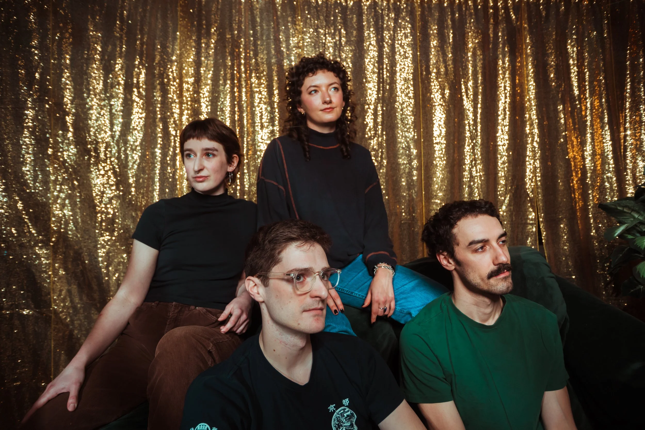 A group of people in front of a gold, sparkly curtain backdrop, posing together with some seated and others standing behind.