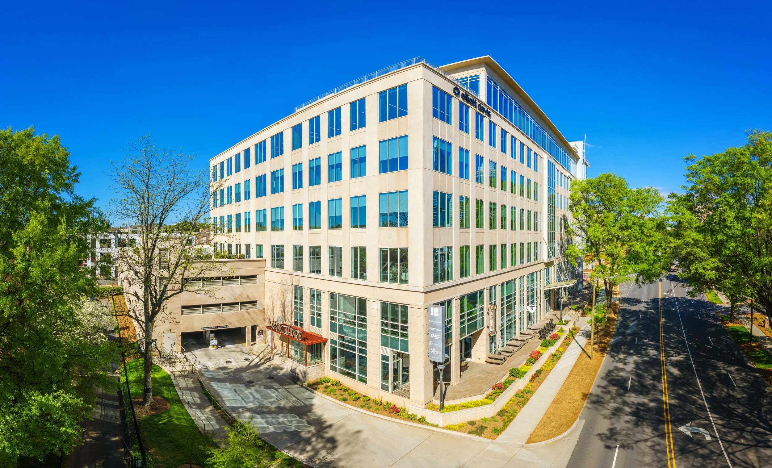Photo of a modern multi-story office building with large glass windows, trees in the foreground, and clear blue sky.