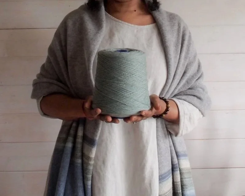 Person holding a large spool of light green yarn in front of a light wooden wall.