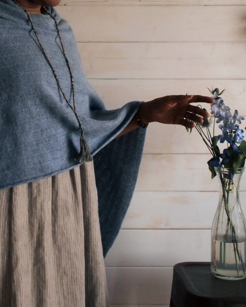 Person placing a flower into a vase with light-colored wooden wall background.