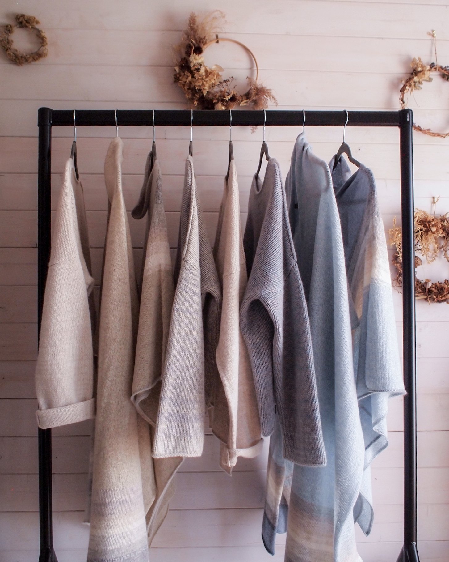 Jules Hogan's  soft light filled studio with paint washed wooden boards on the wall. A rail with the Peace Collection. Soft shades of cream, neutrals smoke grey and dusky blue.