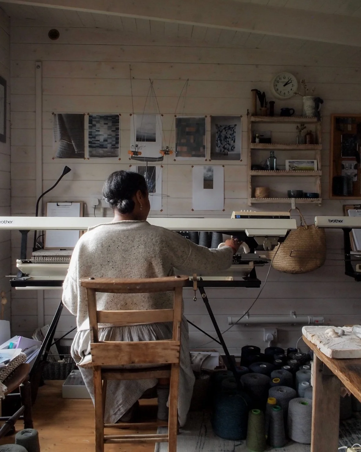 A woman sat on a chair at the knitting machine in her studio.
