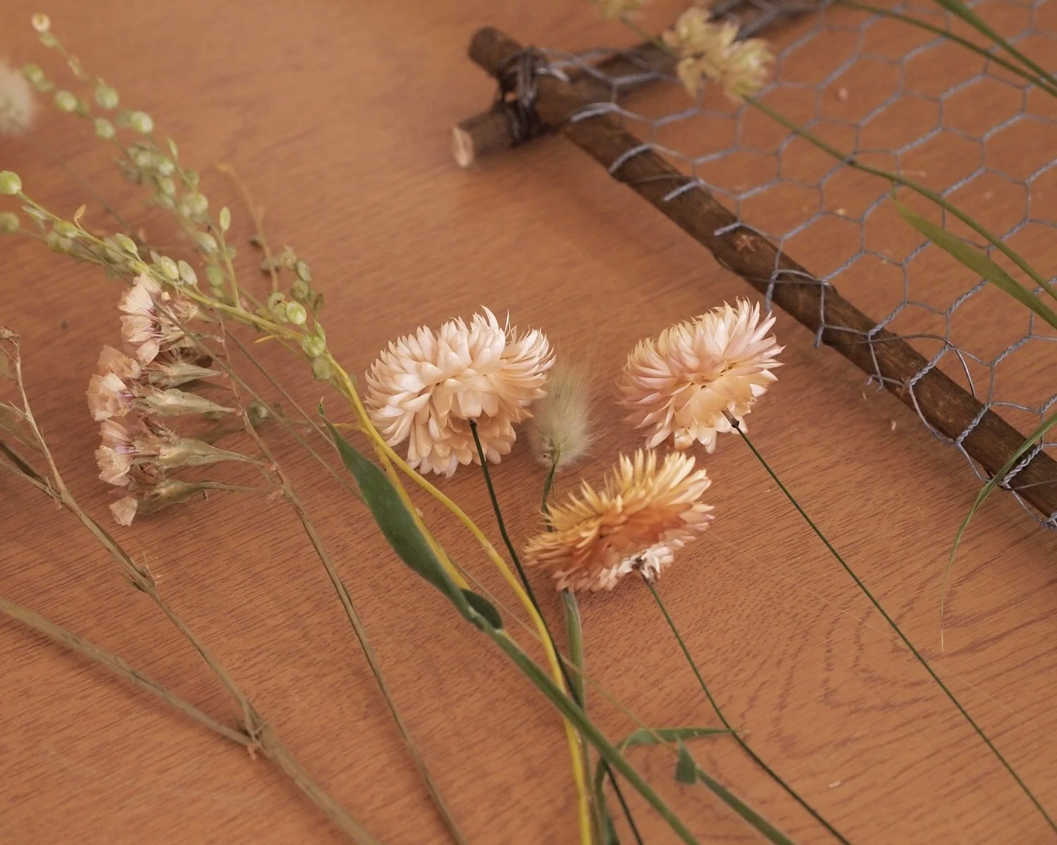 A willow frame, covered in chicken wire, will dried flowers on a wooden table.