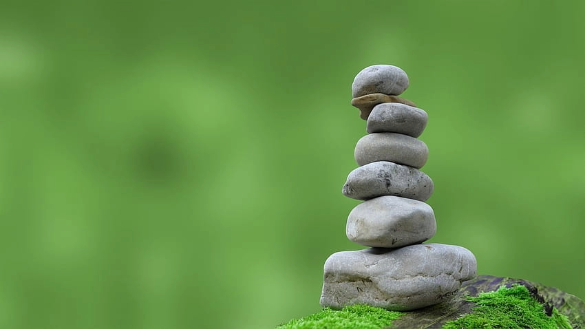 Stacked balanced stones on a log with green moss and blurred green background.