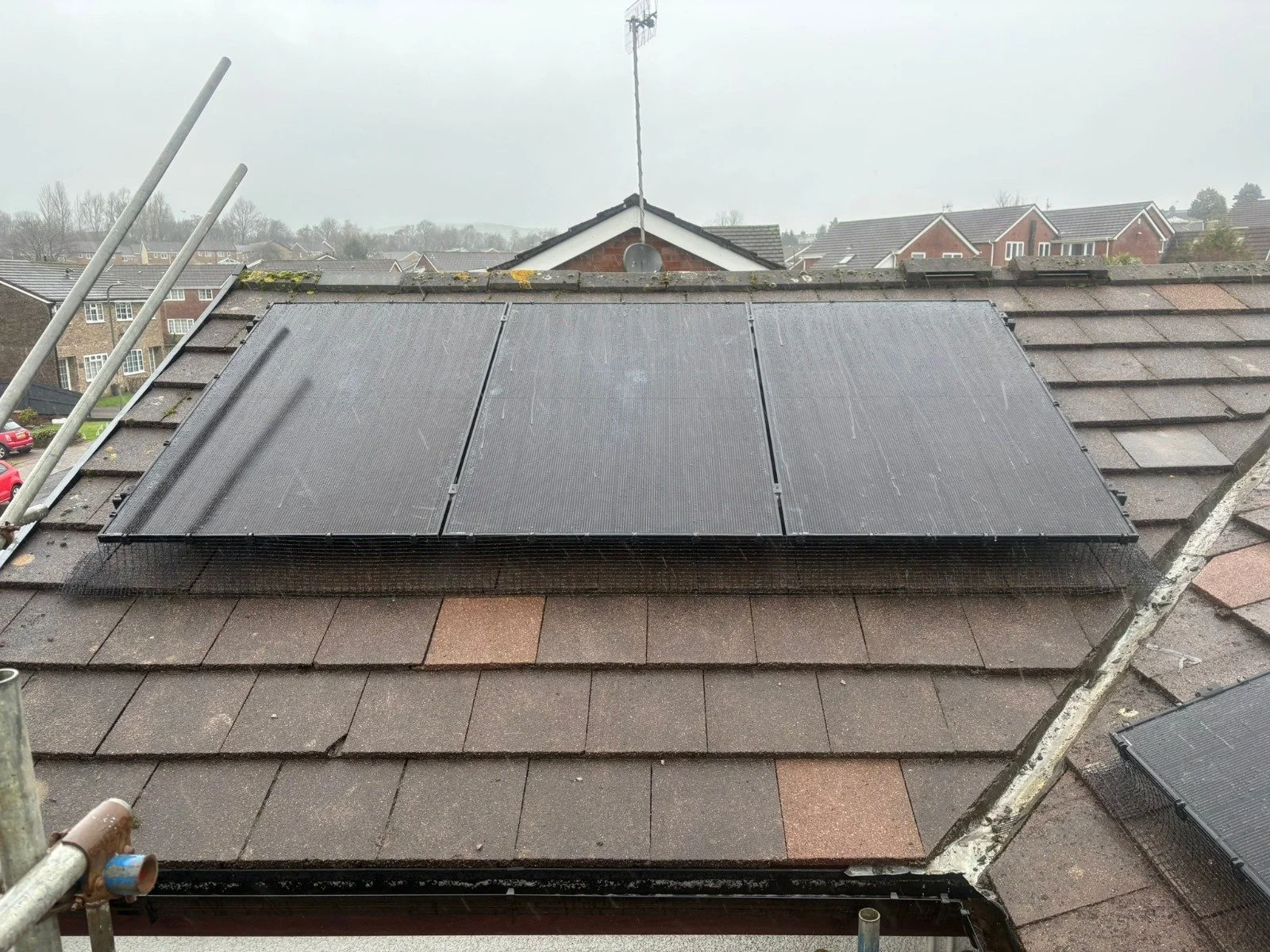 Solar panels installed on a house roof on a cloudy day, with neighboring houses visible in the background.