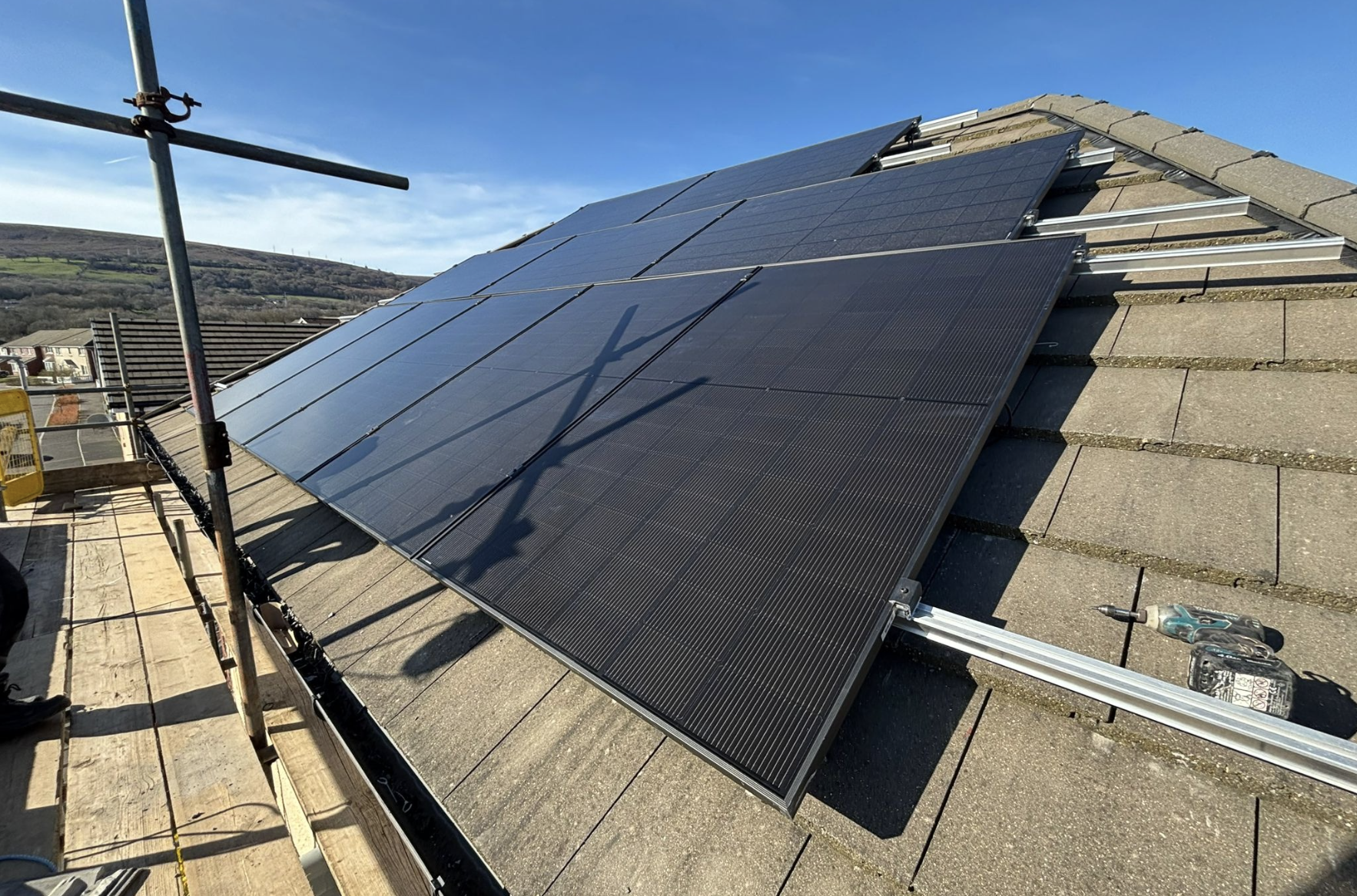 Solar panels installed on a sloped roof under a blue sky, with a flagpole and shadow reflections visible.