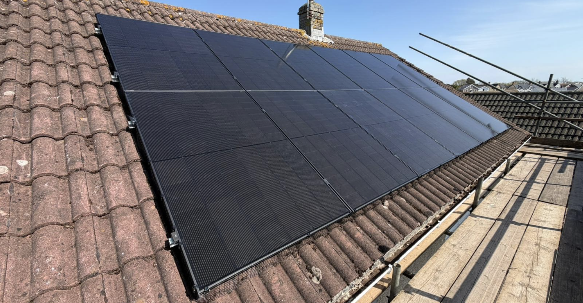 Photograph of a house roof with black solar panels installed on one side.