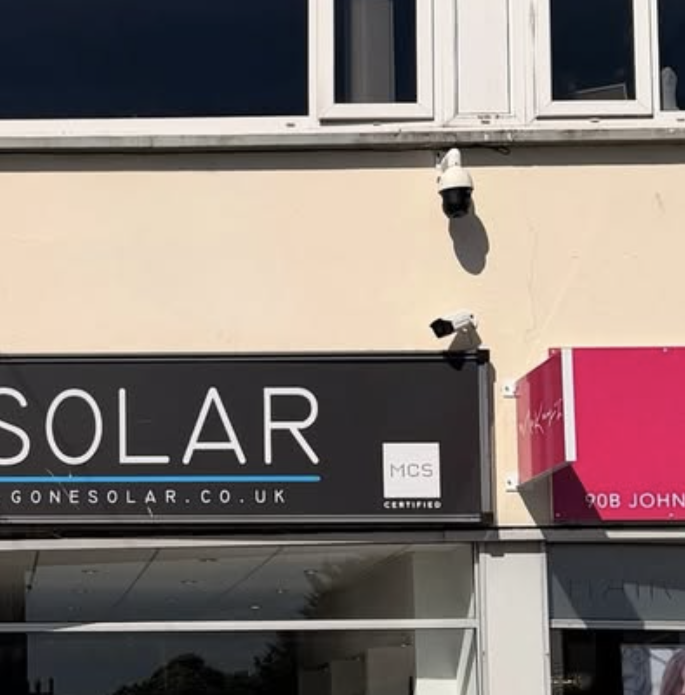 Sign for a solar energy company on the building exterior with security cameras nearby.