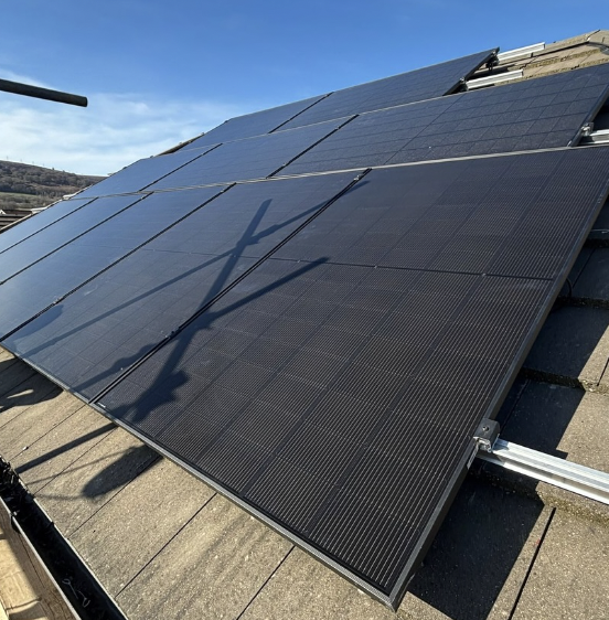 Photograph of black solar panels installed on a rooftop under a clear blue sky.