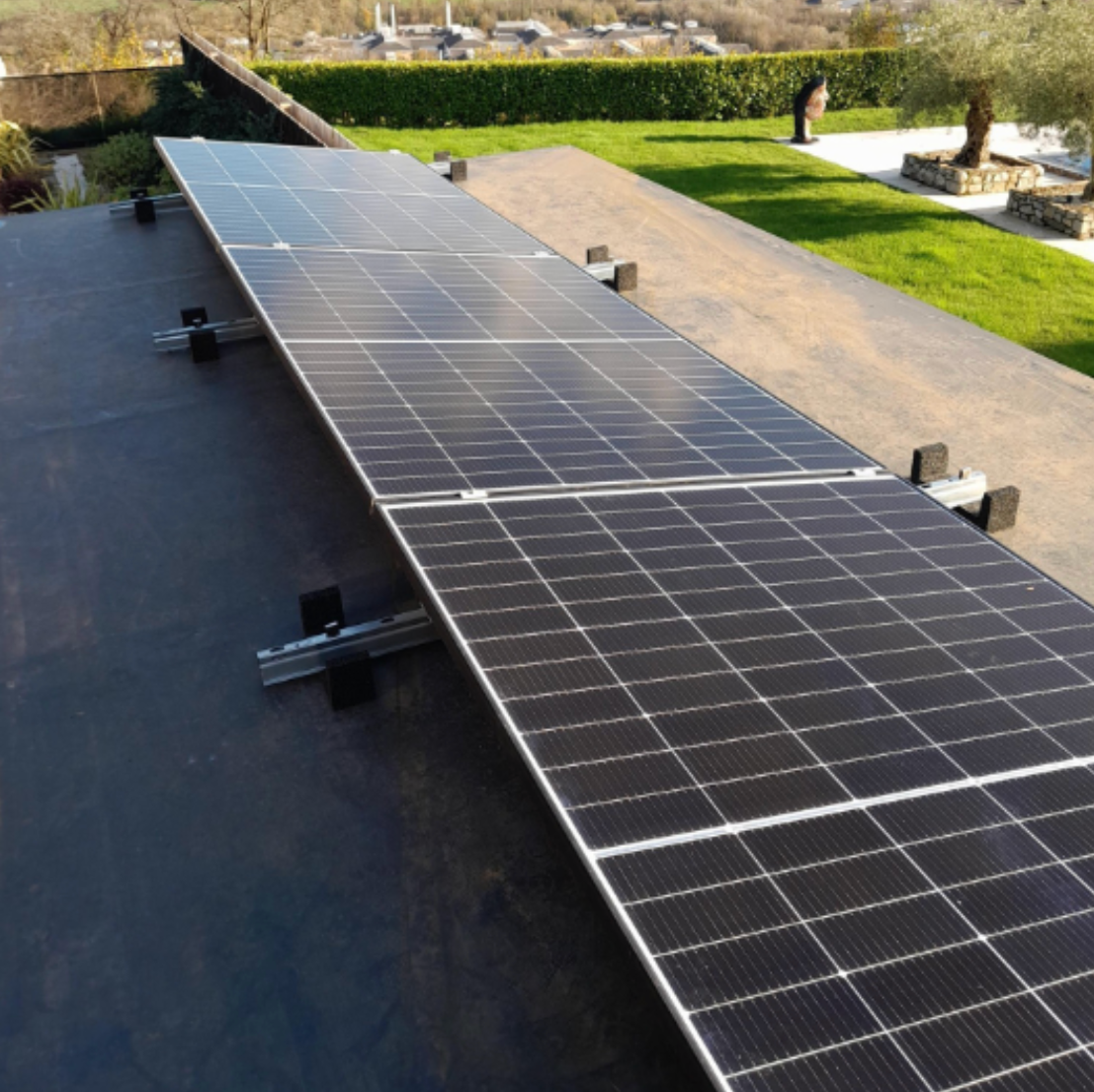 Solar panels installed on a rooftop with a backyard and green lawn in the background.