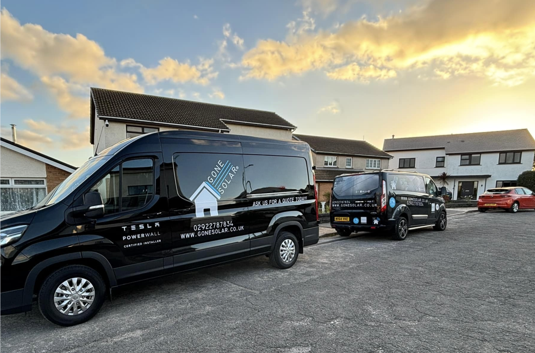 Two black delivery vans parked on residential street during sunset. The larger van has GONE SOLAR branding, including a house logo, website, and contact information. The smaller van also features GONE SOLAR branding, with website, phone number, and logo. Houses with white walls and brown roofs are in the background.